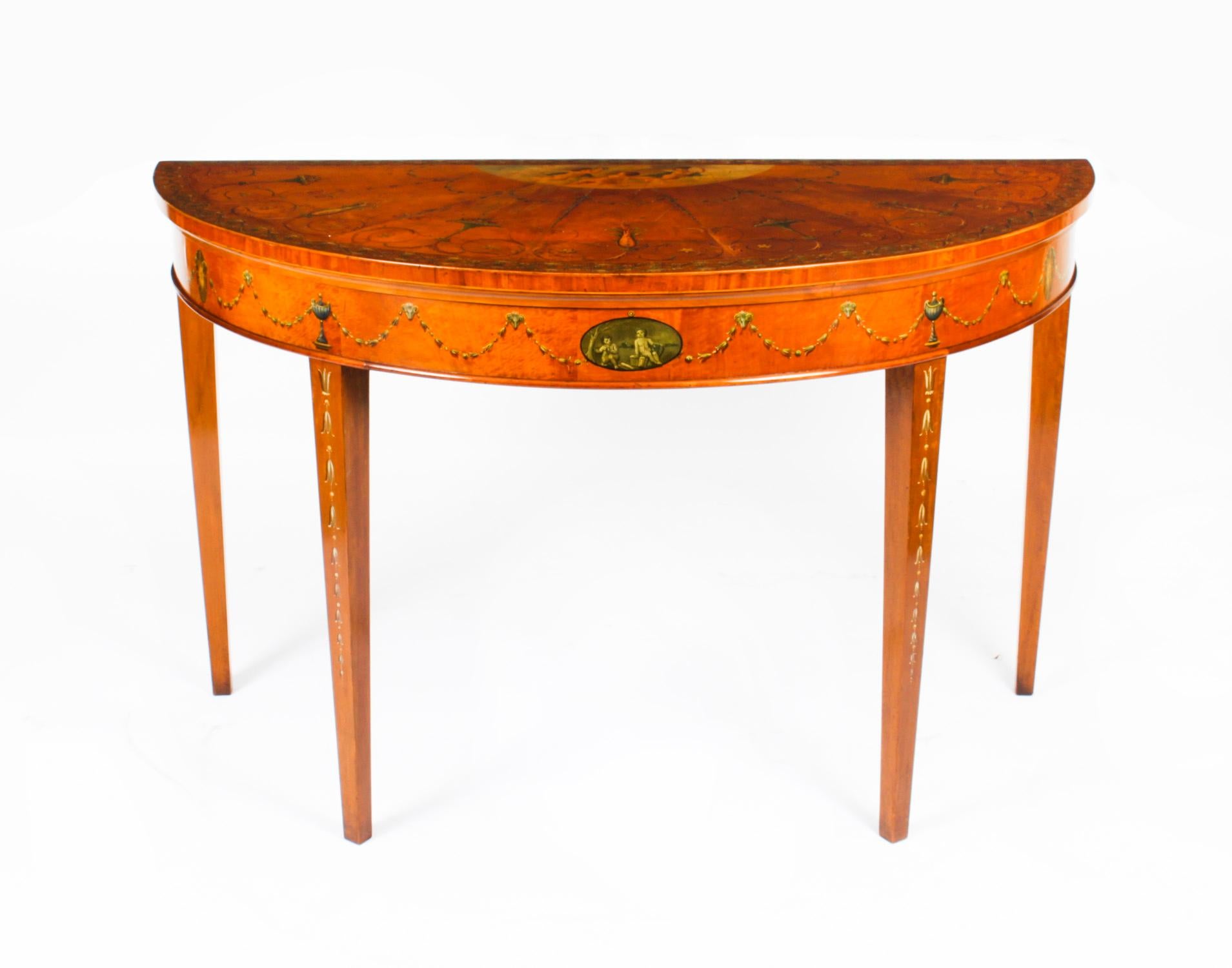 This is a beautiful antique George III hand painted satinwood demi-lune console table, circa 1780 in date.
 
The console is beautifully decorated with hand painted cherubs, floral, foliate and ribbon-tied flowering swags in the manner of Angelica