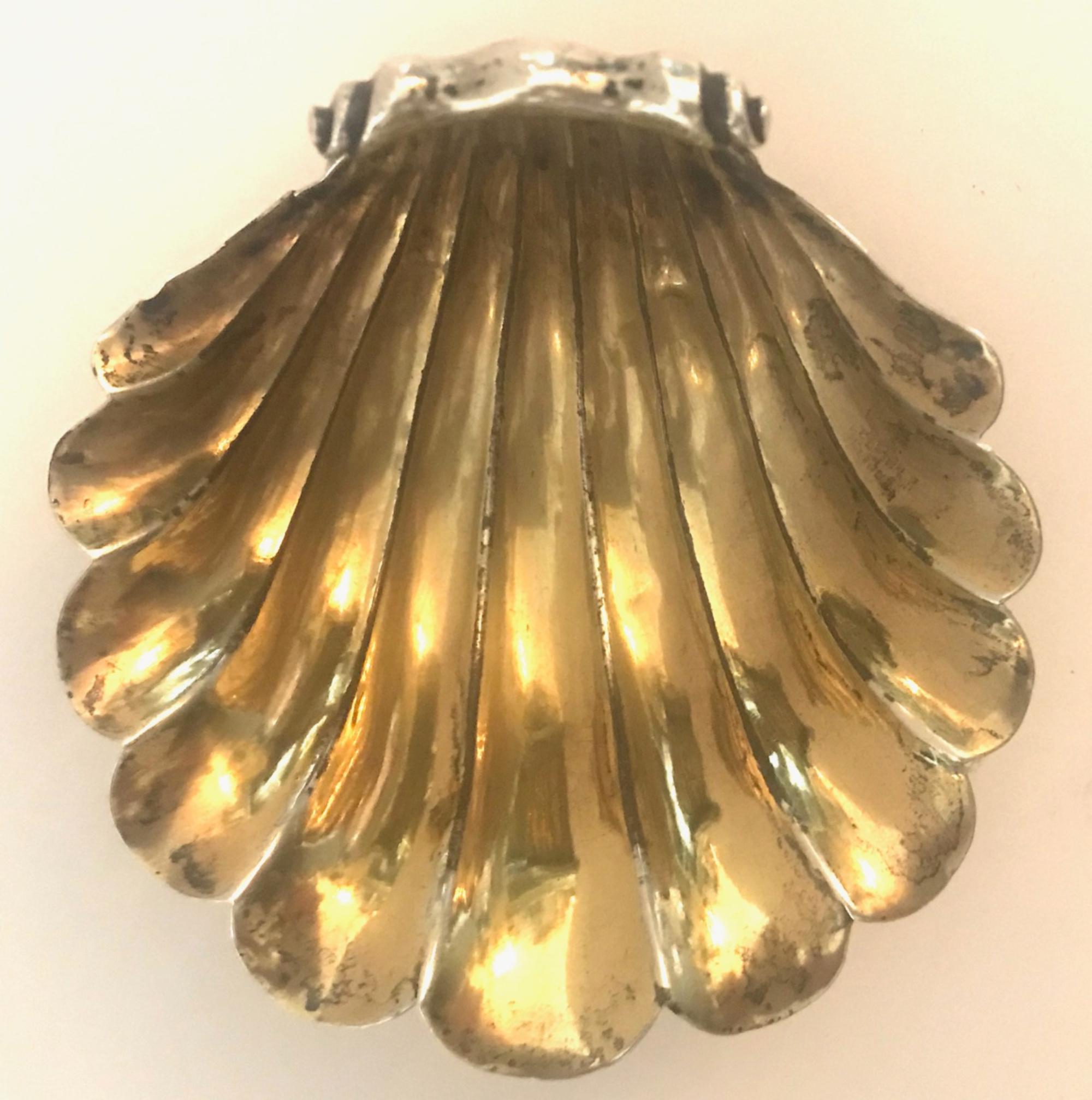 Antique George III silver scallop shell butter dish, 1790

A magnificent Georgian silver cast scallop shell butter dish with curled handle. The rolled over end is engraved with a family bear crest. This handsome shell dish sits on three cast conch