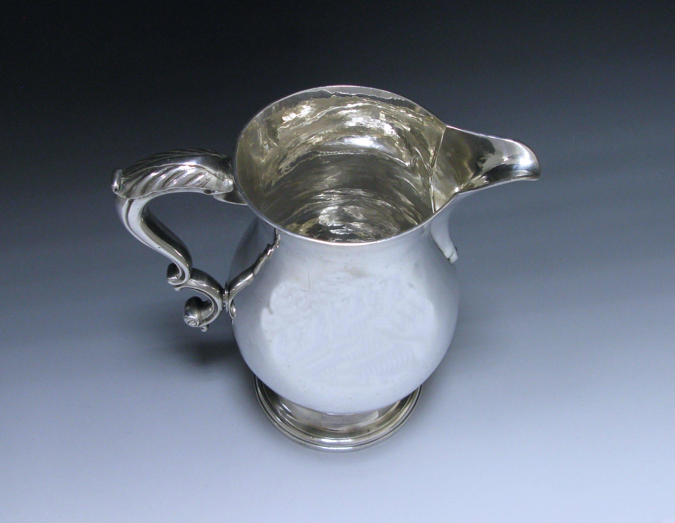 A magnificent antique George III sterling silver beer / water jug is of plain baluster form onto a circular spreading foot. The jug has a cast sterling silver S scroll handle ornamented with a scrolling leaf design. The beak style spout is