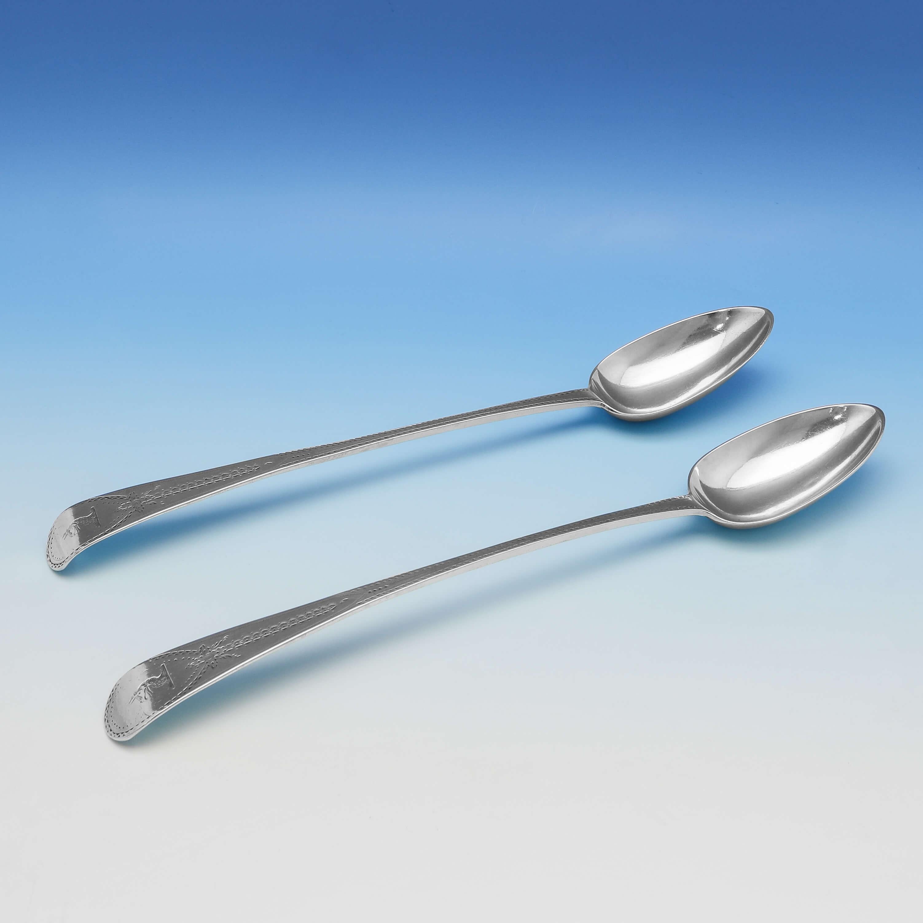 Hallmarked in London in 1788 by Henry Hobdell, this striking, George III, antique sterling silver pair of basting spoons, feature wonderful neoclassical style bright cut engraved decoration throughout, and engraved crests. Each basting spoon