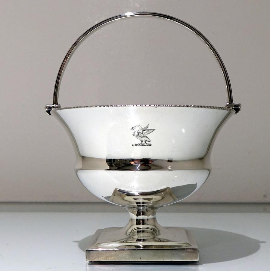 A very fine and highly collectable silver swing handled sugar basket decorated with an upper gadroon border and a reed designed handle. The foot is square raised pedestal and there are two contemporary crests (one regimental) on the centre front and