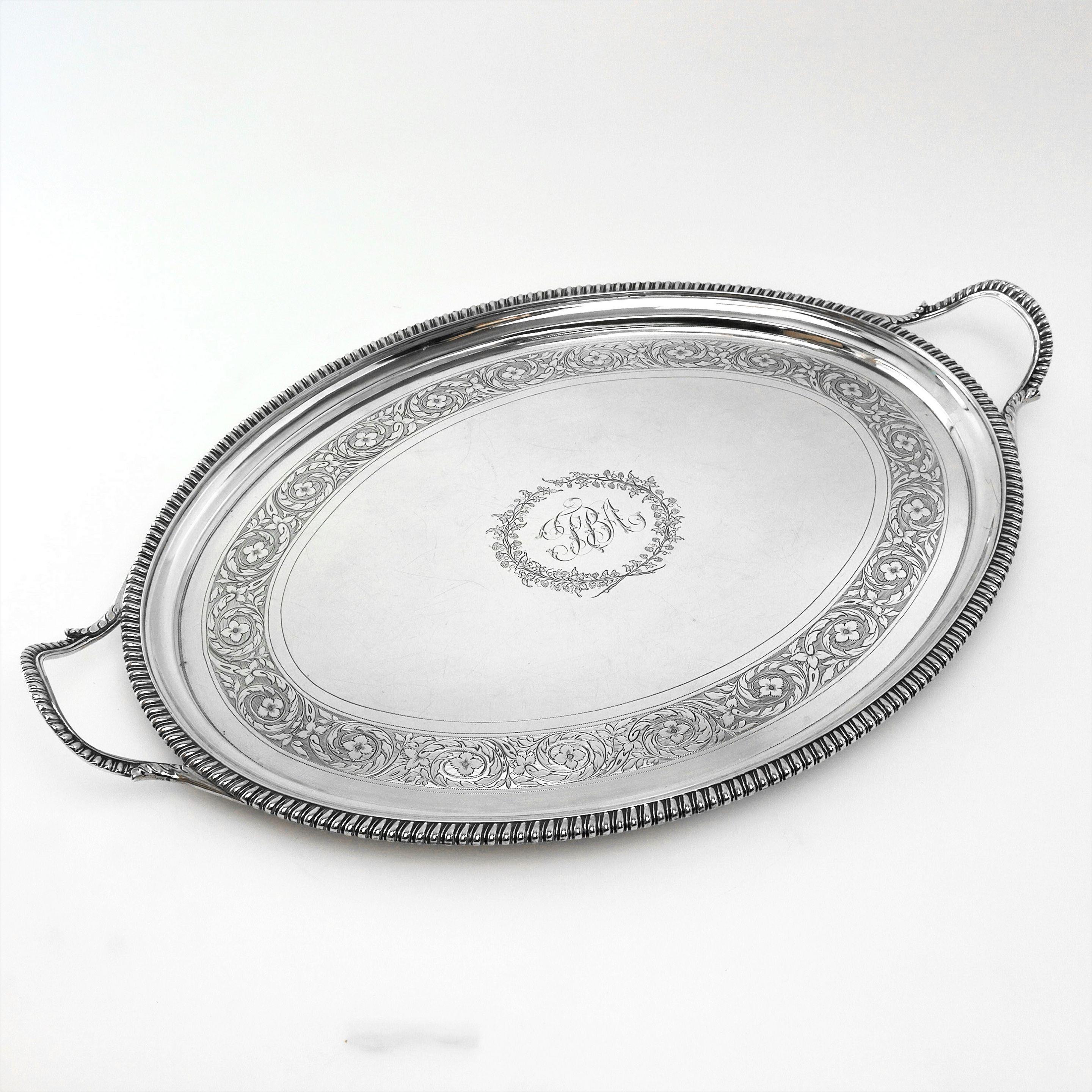 A classic antique Georgian solid Silver Tea Tray with an oval shape and decorated with a gadroon border on the rim and on the handles. The interior of the Tray has an engraved floral and scroll band around a central cartouche with initials in the