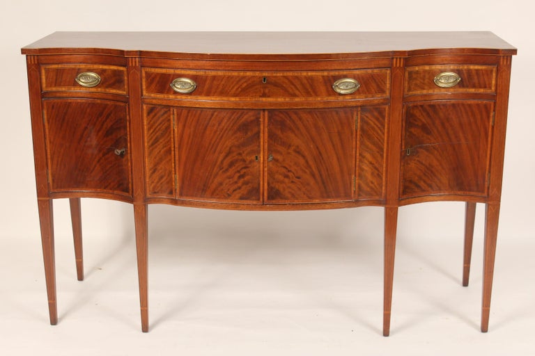 Antique George III style mahogany serpentine shaped sideboard, early 19th century. With a serpentine shaped front having three flame mahogany and cross banded drawers and four flame mahogany and cross banded doors, resting on square tapered legs.