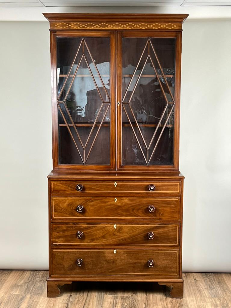 A handsome George IV mahogany stepback bookcase, dating to around 1830, crafted in the refined neoclassical tradition of early 19th century England. The upper cabinet features striking geometric astragal glazing bars forming bold diamonds and