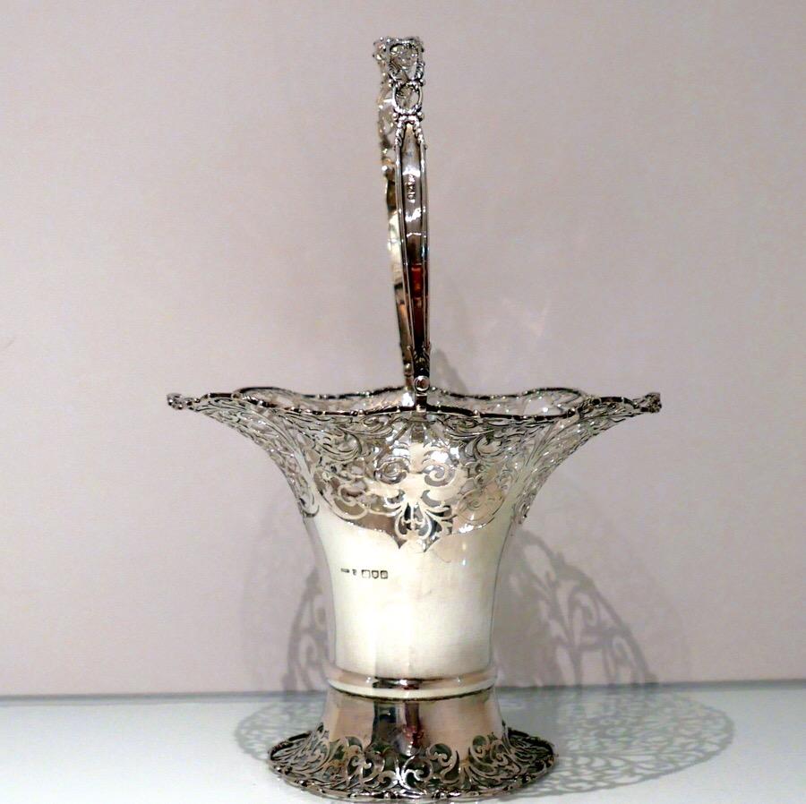 A fine sterling silver elongated vase shaped swing handled flower basket decorated with upper and lower elegantly intricate hand piercing. The upper bowl of the basket fans out for decorative highlights and the centre section is plain formed in