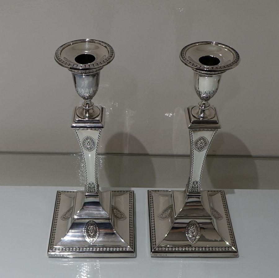 A stunning pair of square based silver candlesticks decorated with ornate framed continuing borders and asymmetrical oval floral plaques.