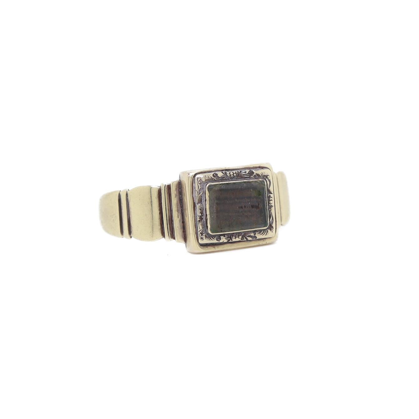A fine antique mourning ring.

In 14 karat yellow gold.

With braided hair under a beveled bezel-set glass bezel.

The center-set bezel section surrounded by embossed floral work. The band with stepped shoulders and a taper to the shank.

In the