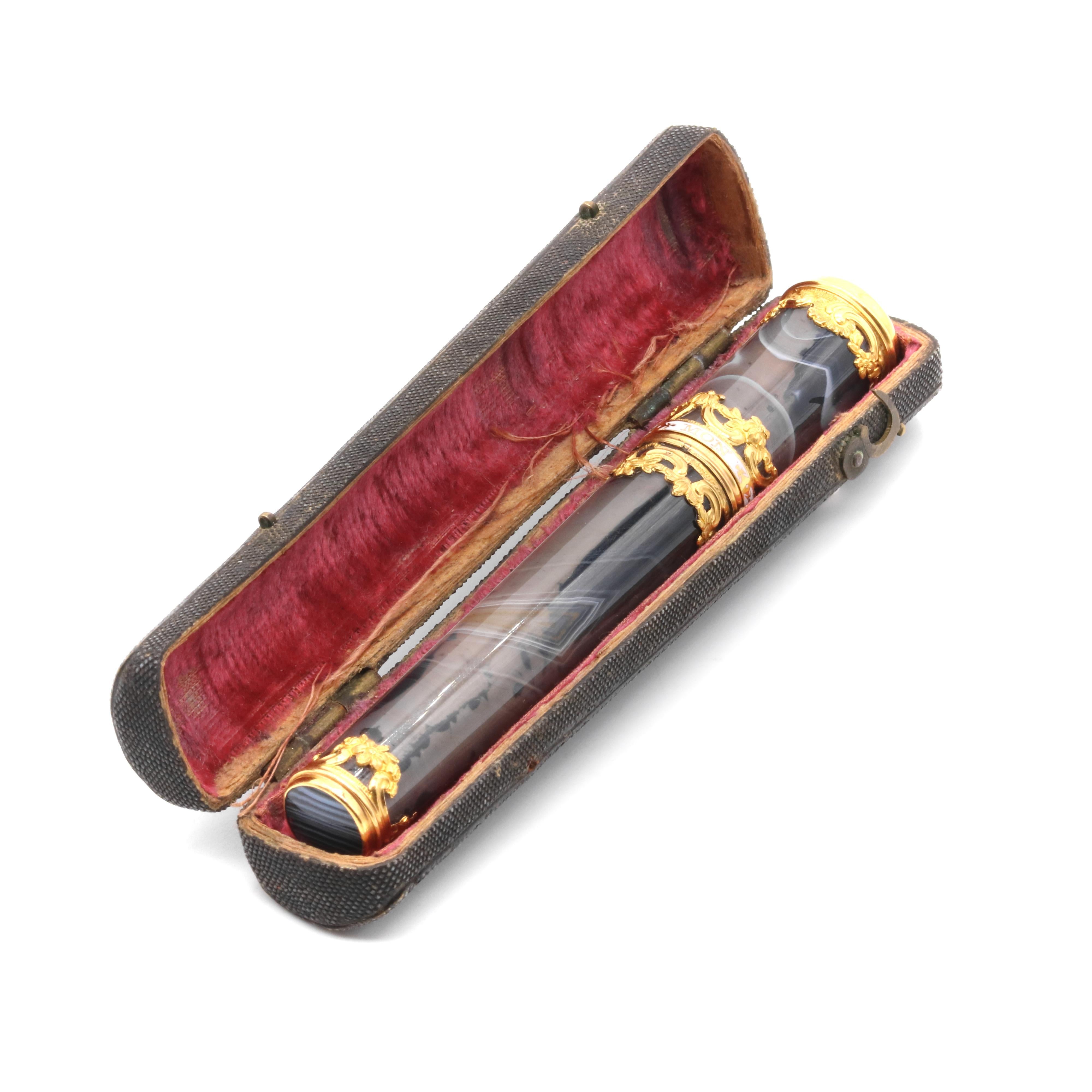 A Georgian gold, enamel and agate needle case or etui, comprising a needle case in polished grey agate, with an inscription in white enamel, with floral detailing in 18 karat yellow gold. 

This striking Georgian etui is truly beautiful to behold