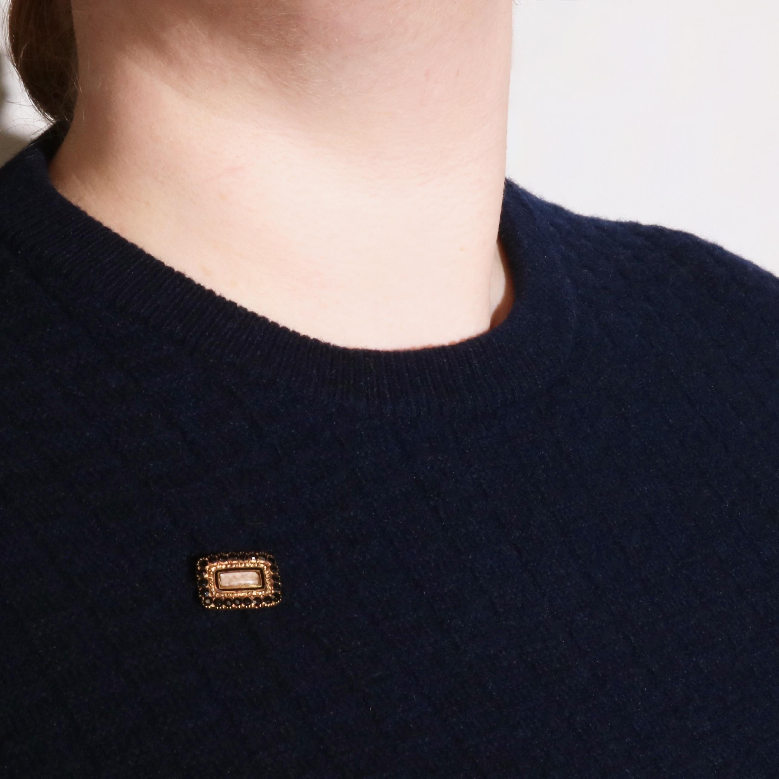 An antique yellow gold brooch, comprising twenty-two round cut black paste stones, black enamel, and one panel of glass, set in 18 karat yellow gold, with a silver pin. 

The brooch is rectangular in shape, and has a glass covered compartment,