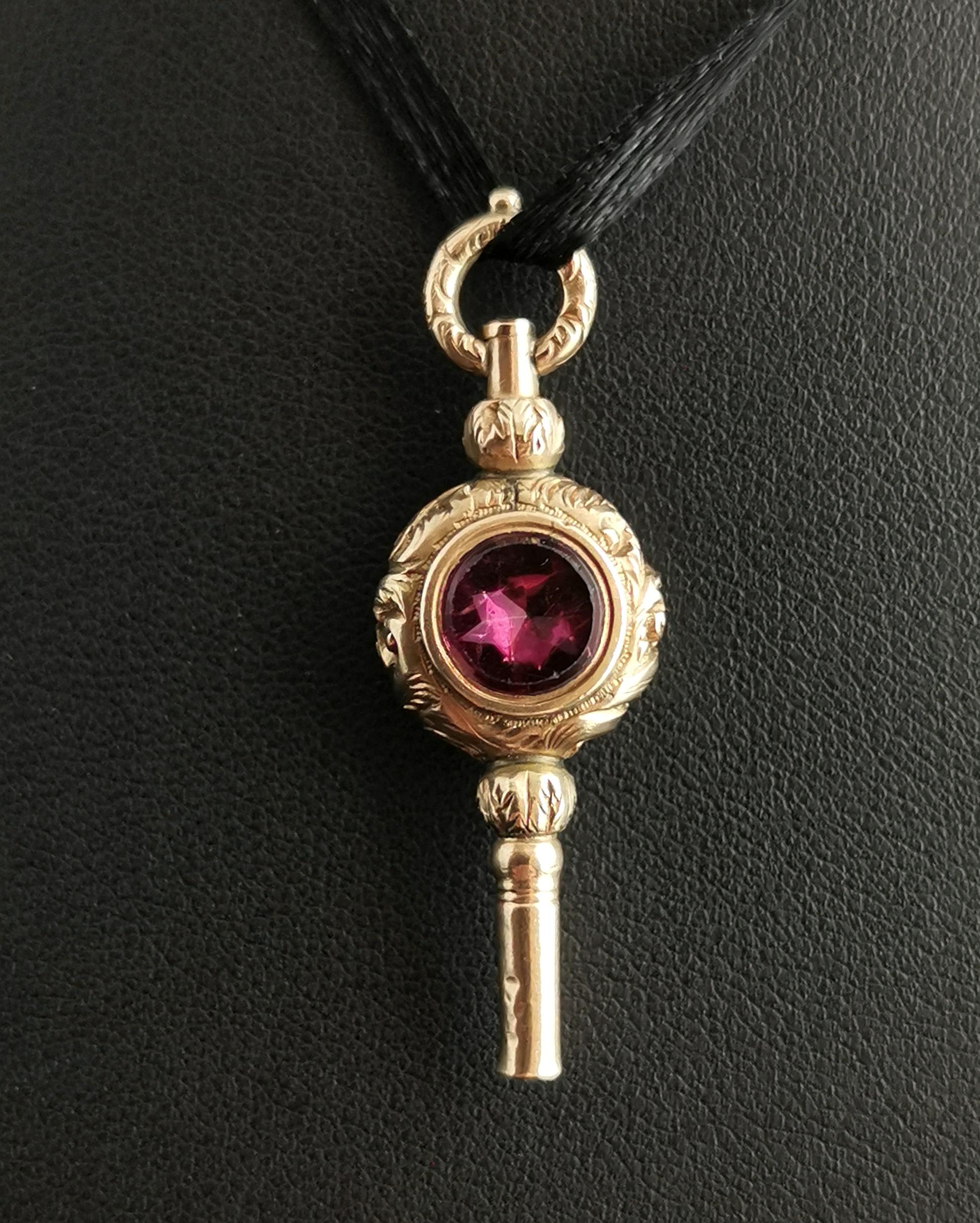 A beautiful antique late Georgian 9kt yellow gold watch key.

The key is cased in chased and engraved 9kt gold with a round flat cut gemstone to the front and back.

It is a larger sized watch key and makes a wonderful and interesting pendant, it is
