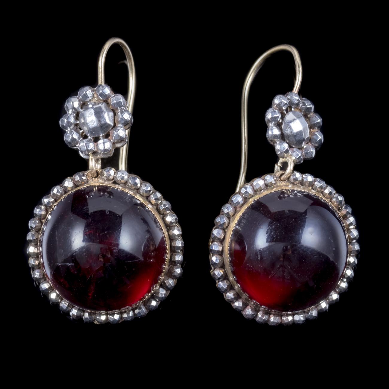 A spectacular pair of antique Georgian earrings boasting two large cabochon Paste stones which have the dark red allure of Garnet’s and look like the real thing. The stones are bordered with faceted Cut-Steel studs which were common in the Georgian