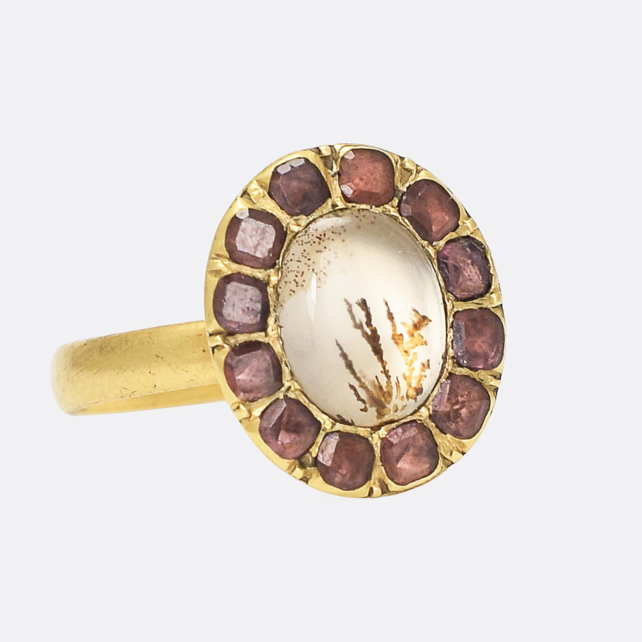 A beautiful Georgian dendritic agate picture frame ring. The principal stone displays fern-like markings, and has been foil-backed creating a hazy white glow as the light reflects back through it. The agate rests within a frame of flat cut garnets,