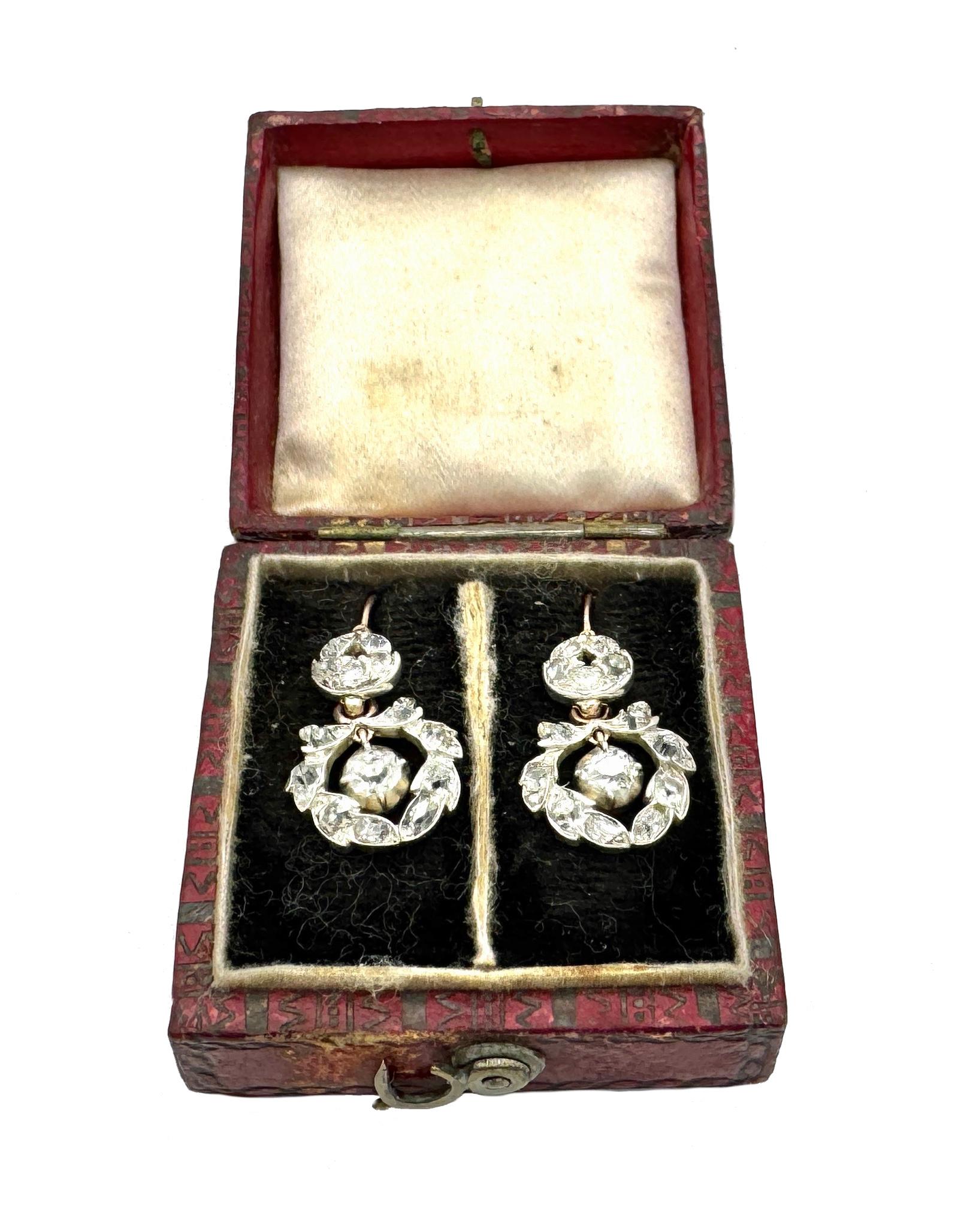 Questi insoliti orecchini pendenti antichi georgiani sono stati creati nel 1820. Gli orecchini sono disegnati a forma di corona d'alloro penzolante. Le corone sono sospese da orecchini superiori con un fiore composto da diversi piccoli diamanti