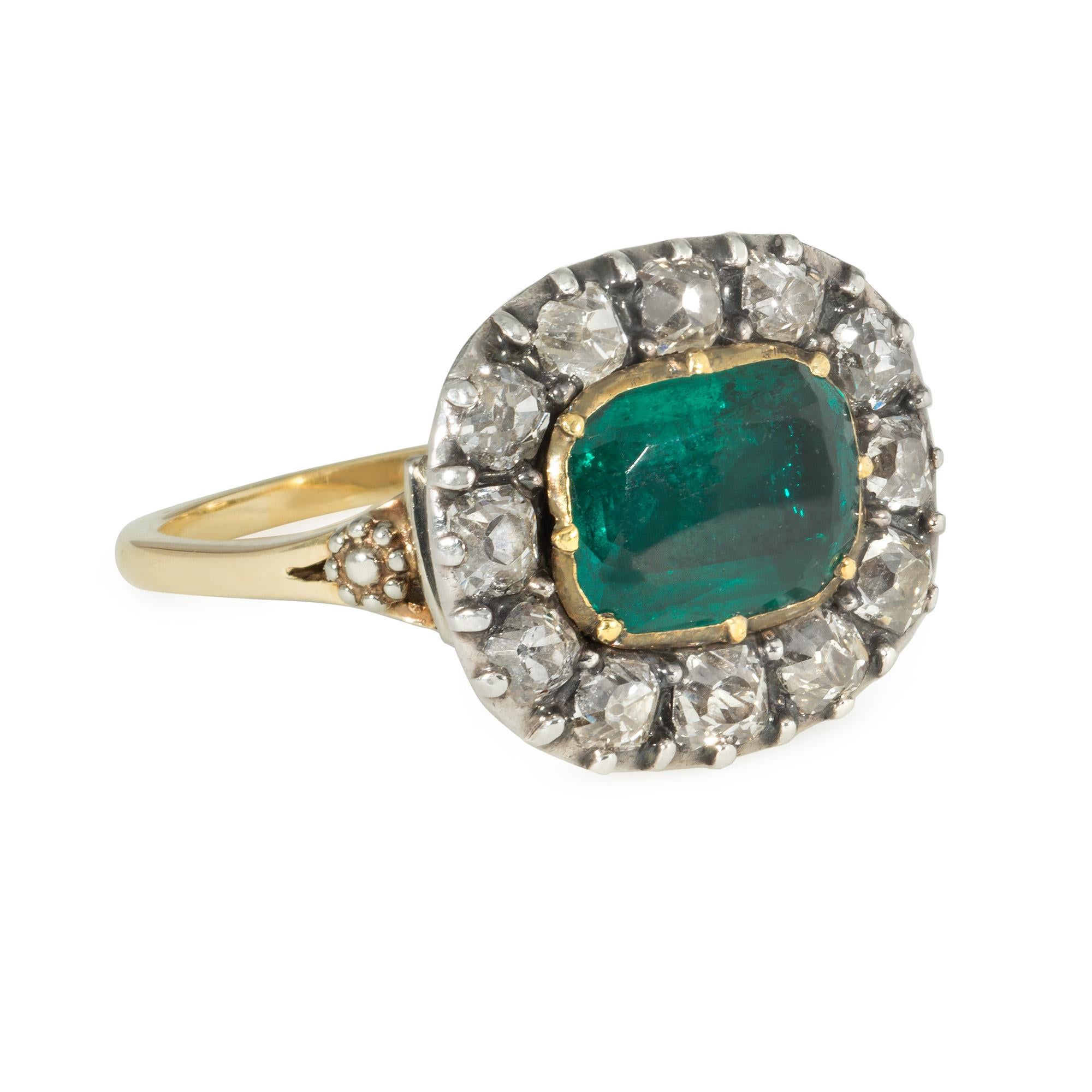 An antique Georgian period old mine cut diamond and emerald cluster ring, in sterling silver and 18k gold closed back mount with silver cluster motifs on the shoulders. Later reshanking.  Atw old mine cut diamonds 0.66 ct., emerald measures