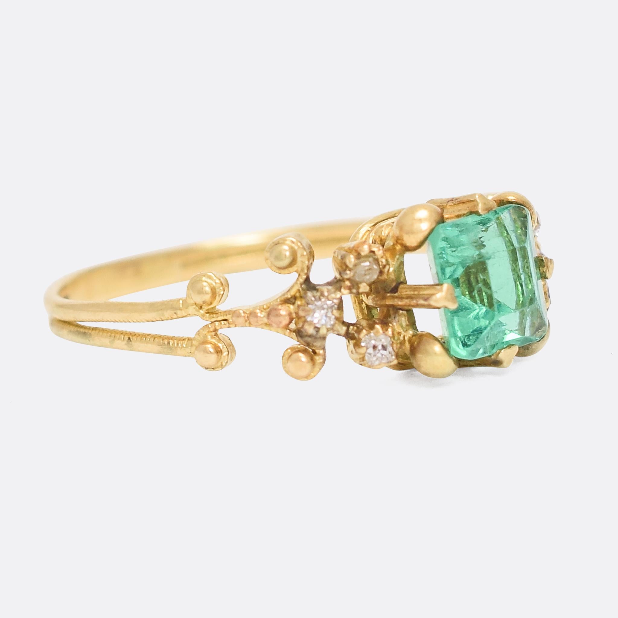 A beautiful Georgian Emerald solitaire ring with exquisite cannetille gold work and diamond accents to the shoulders. The emerald is bright and vibrant, and rests in a crown-like claw mount, and the ring is completed with a simple reeded band. It's