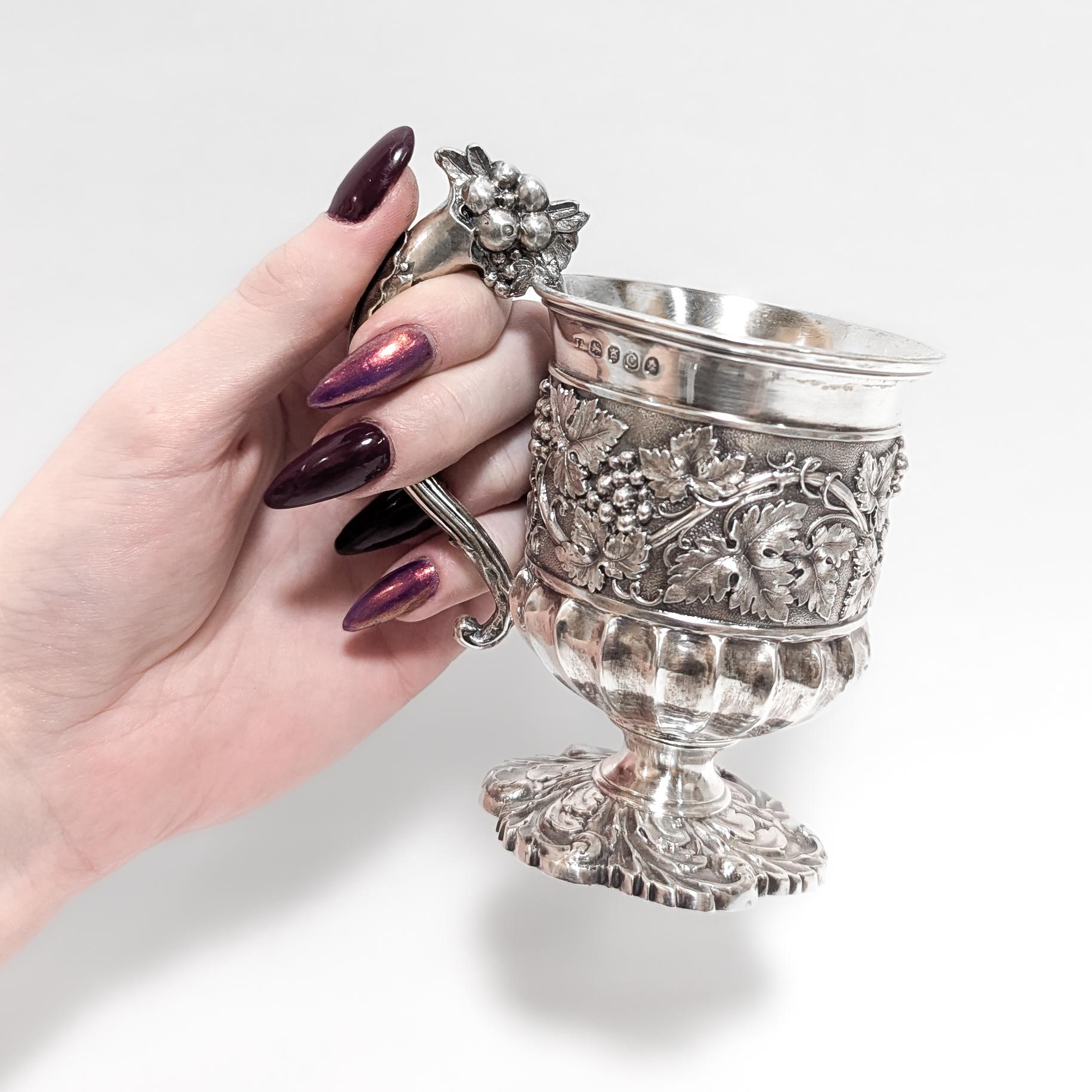 A fine antique English christening cup or mug.

Made by Joseph Angell I of London, England in 1818.

In sterling silver.

With repousse grape vine decoration around the body, a figural cornucopia handle, a gilt interior, and a twisted acanthus leaf