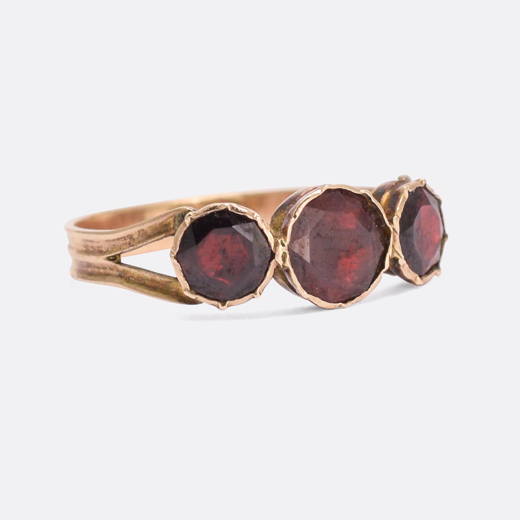 The stunning Georgian three-stone ring is set with foil-backed flat cut garnets and dates from the very early 19th Century. It's crafted in 9 karat rose gold, with simple split shoulders and a reeded band. The stones display great vibrance and