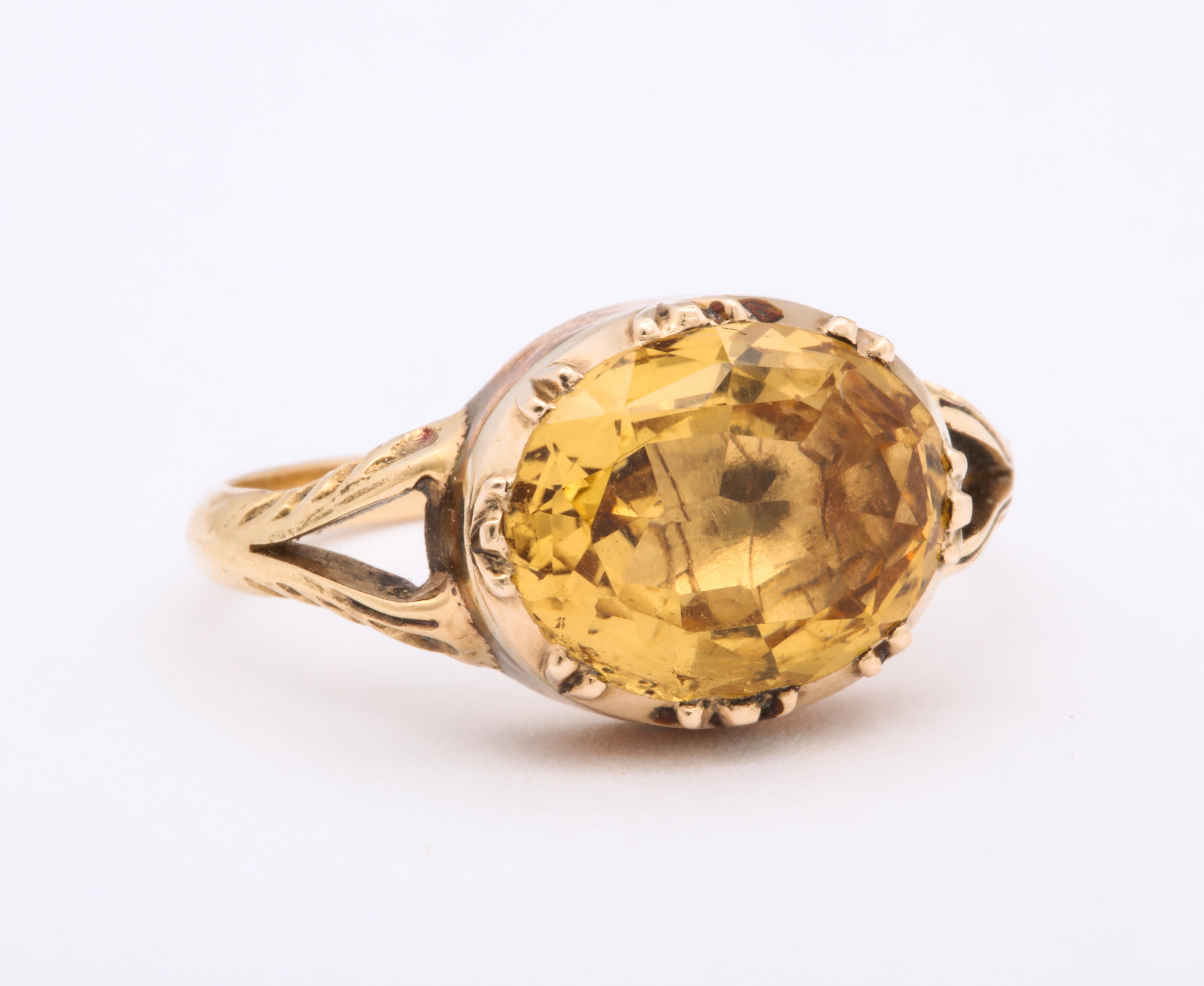 Firmly set In 15 Kt gold triple claw prongs, the oval 4 Ct topaz rests warmly glowing the color of clover honey. Georgian, and in fine condition, this ring has a shank that is doubled at the shoulders as it attaches to a deeper gold foiled closed