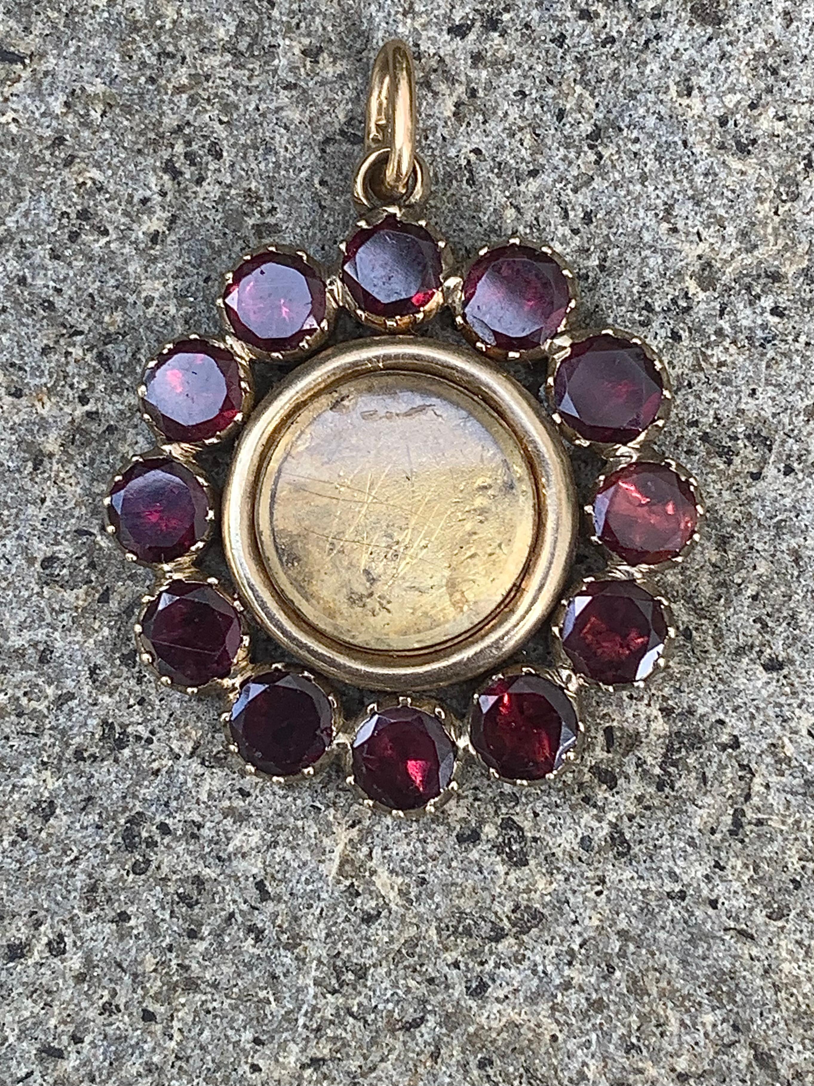 This Georgian pendant has been handcrafted out of 14K yellow and rose gold towards the end of the 18th century. It is designed as a stylized flower with twelve flower petals. Each petal is set with a flat cut round garnet. All garnets are in closed