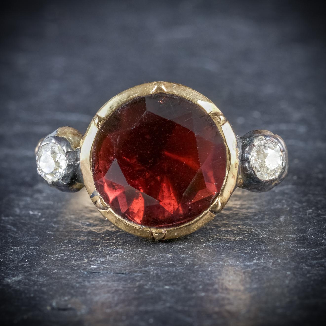 This striking antique Garnet ring is a genuine Georgian piece, Circa 1800

Adorned with a deep red 4ct Garnet in the centre, flanked by two old cut 0.10ct Diamonds

Set in a closed backed 18ct Yellow Gold gallery which is beautifully engraved around