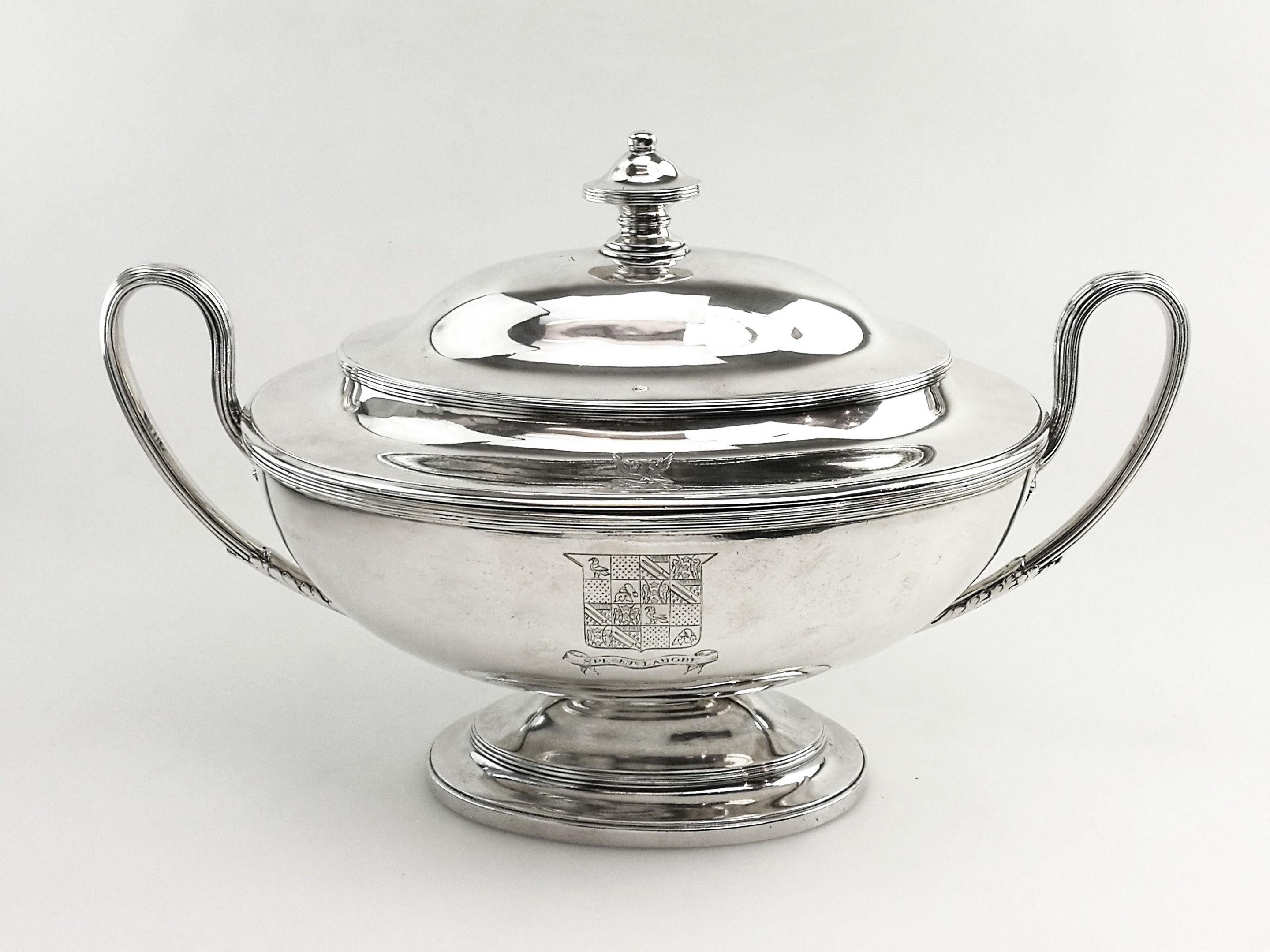 A classic Antique George III Georgian Sterling Silver Soup Tureen in an oval form with two substantial reeded loop handles. The Tureen stands on an oval spread foot and has an impressive domed lid with an oval finial. There is a crest engraved on