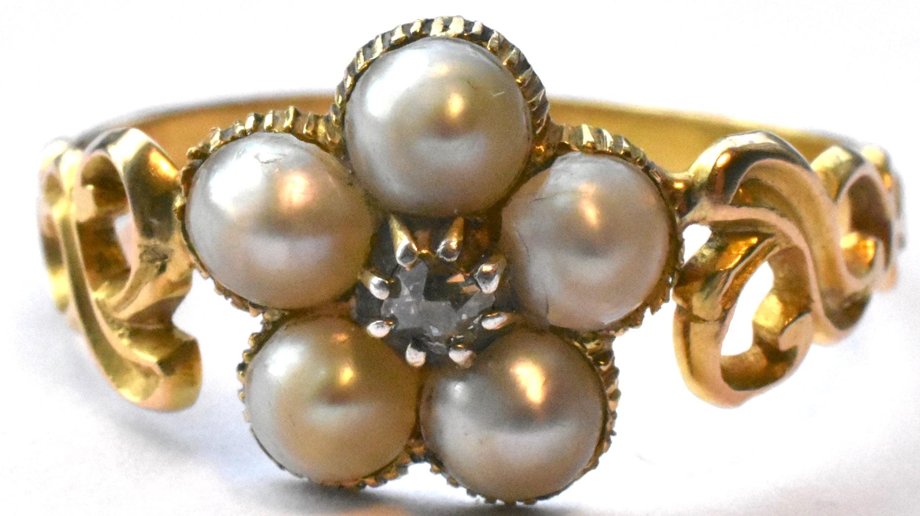 A Georgian period 18K cluster ring in the form of a daisy with 5 seed pearls and a single cushion cut diamond at the center. Incised designs along the band and whirls at the shoulders adorn this ring. It looks as though there may have been a locket