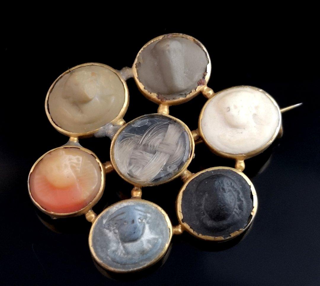 An interesting and rare, antique Georgian Lava cameo mourning brooch.

Oval shaped with a number of small oval cameos set into an 18kt yellow gold setting, they span with a cartwheel effect to a central glazed panel with a plait of light brown