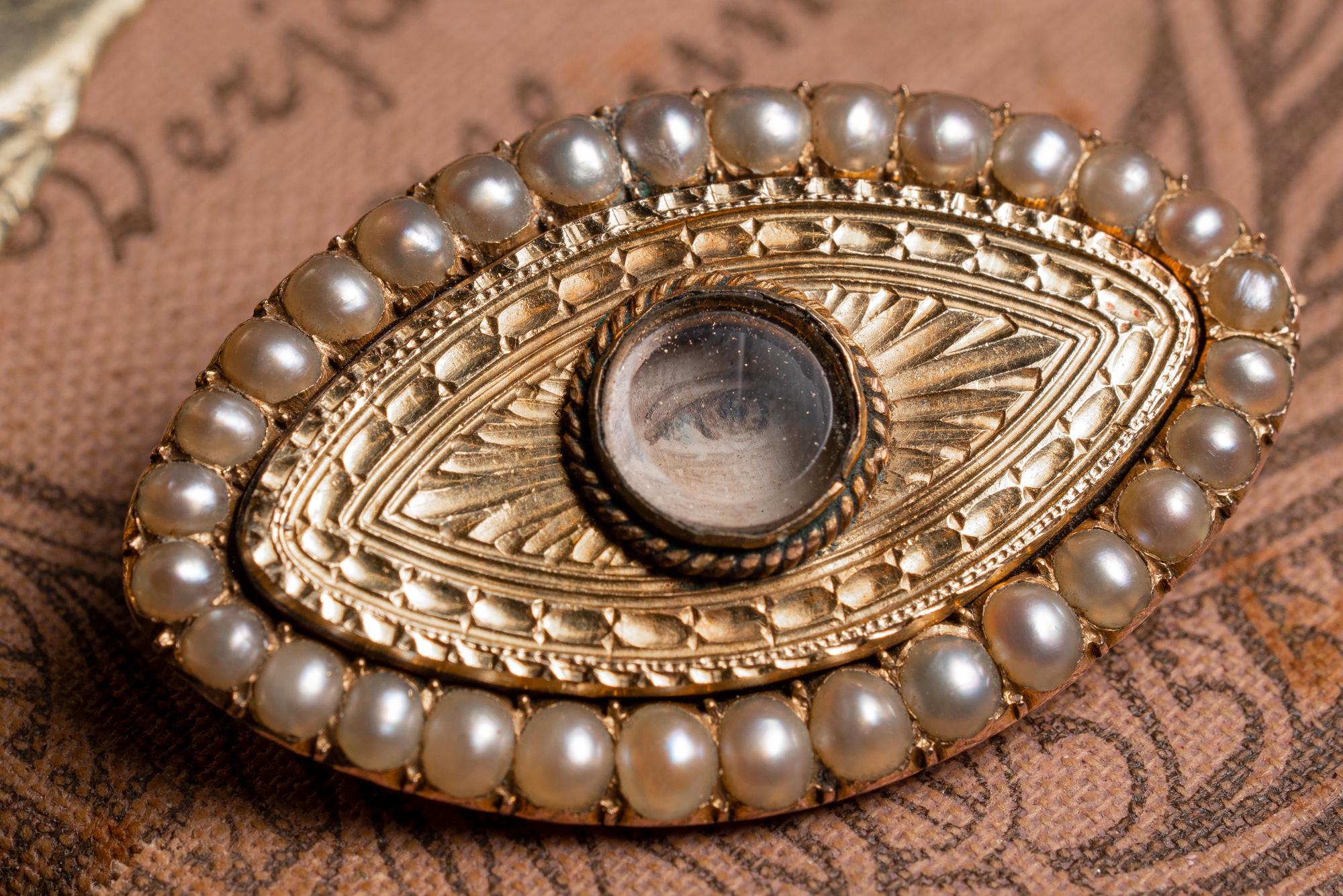 A unique and very rare authentic 'lovers eye' brooch. Made of solid 9kt gold, British. Dating back to the early 1800's and set with original seed pearls, this brooch is set with a crystal centerpiece. The crystal holds a miniature painting of an eye