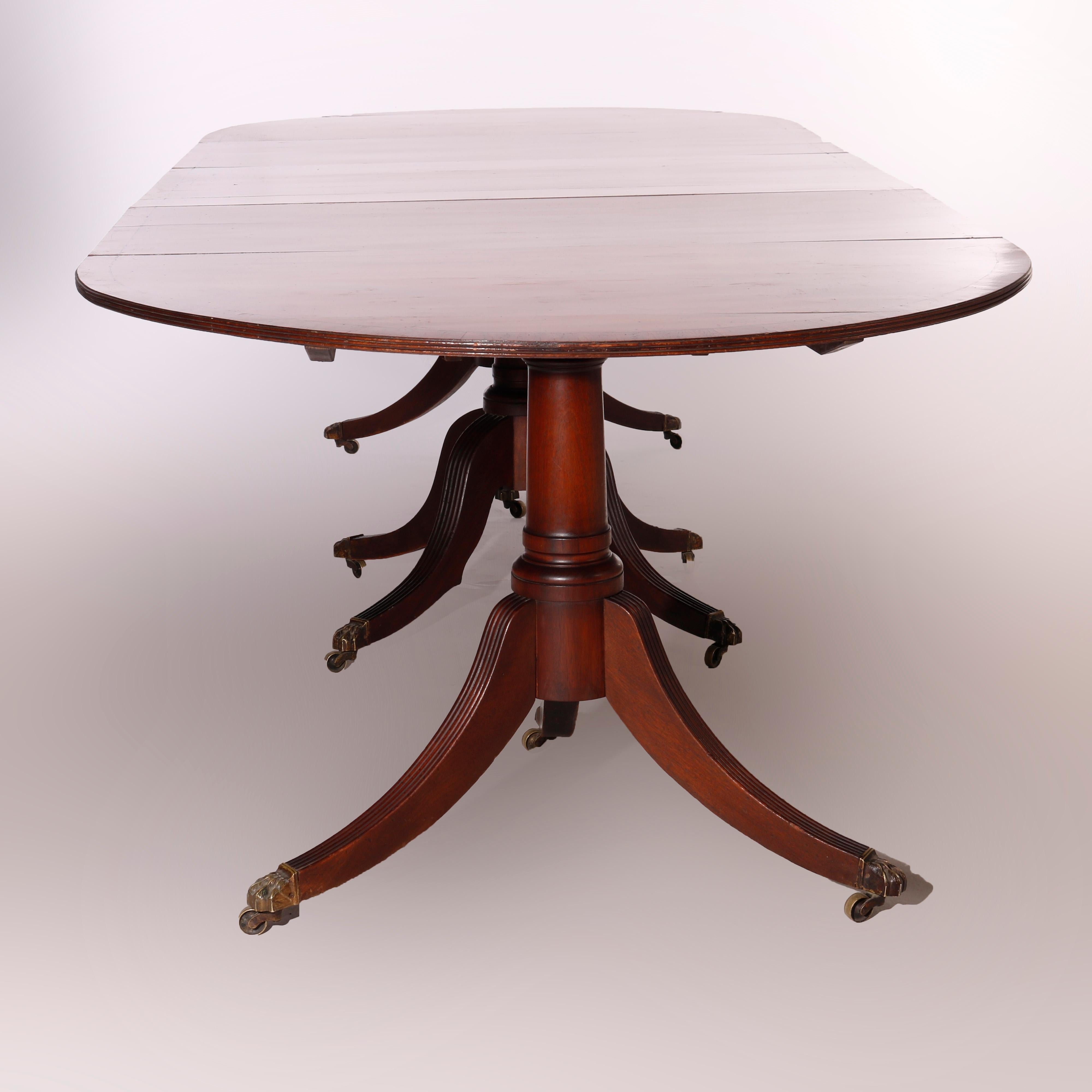 An antique Georgian style dining table offers mahogany construction with cross banded top having ebonized banding raised on reeded convex legs, separates into three parts and accommodates two leaves, 19th century

Measures - without leaves 29''H x