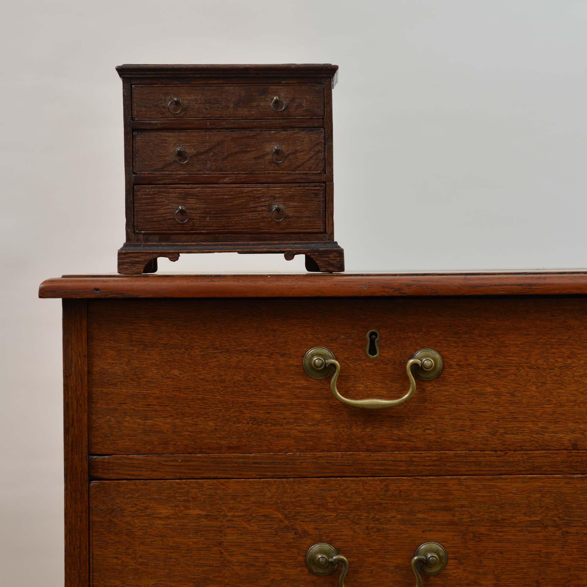 Una cassettiera georgiana in miniatura in Oak
Piano rettangolare lucido con bordo sagomato a tre cassetti graduati su base a gradini con piedi a staffa.  I dettagli sono molto belli se si considera che si tratta di una miniatura, i piedi a staffa