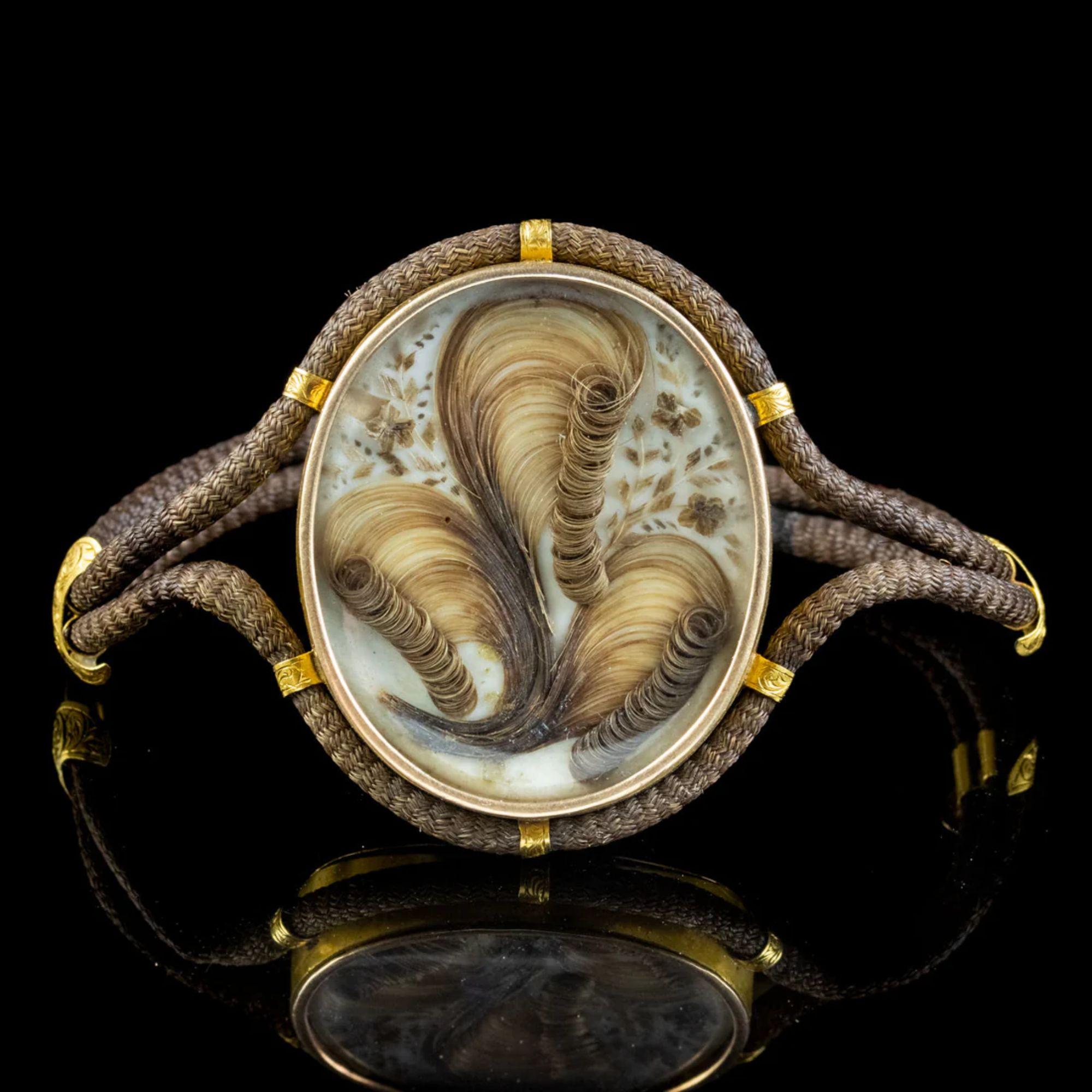A fascinating Antique Georgian Mourning bracelet from the early 19th Century featuring a large 18ct Gold double-sided locket with a magnificent display of curled hair and forget me nots beautifully preserved behind a glass window. 

Mourning
