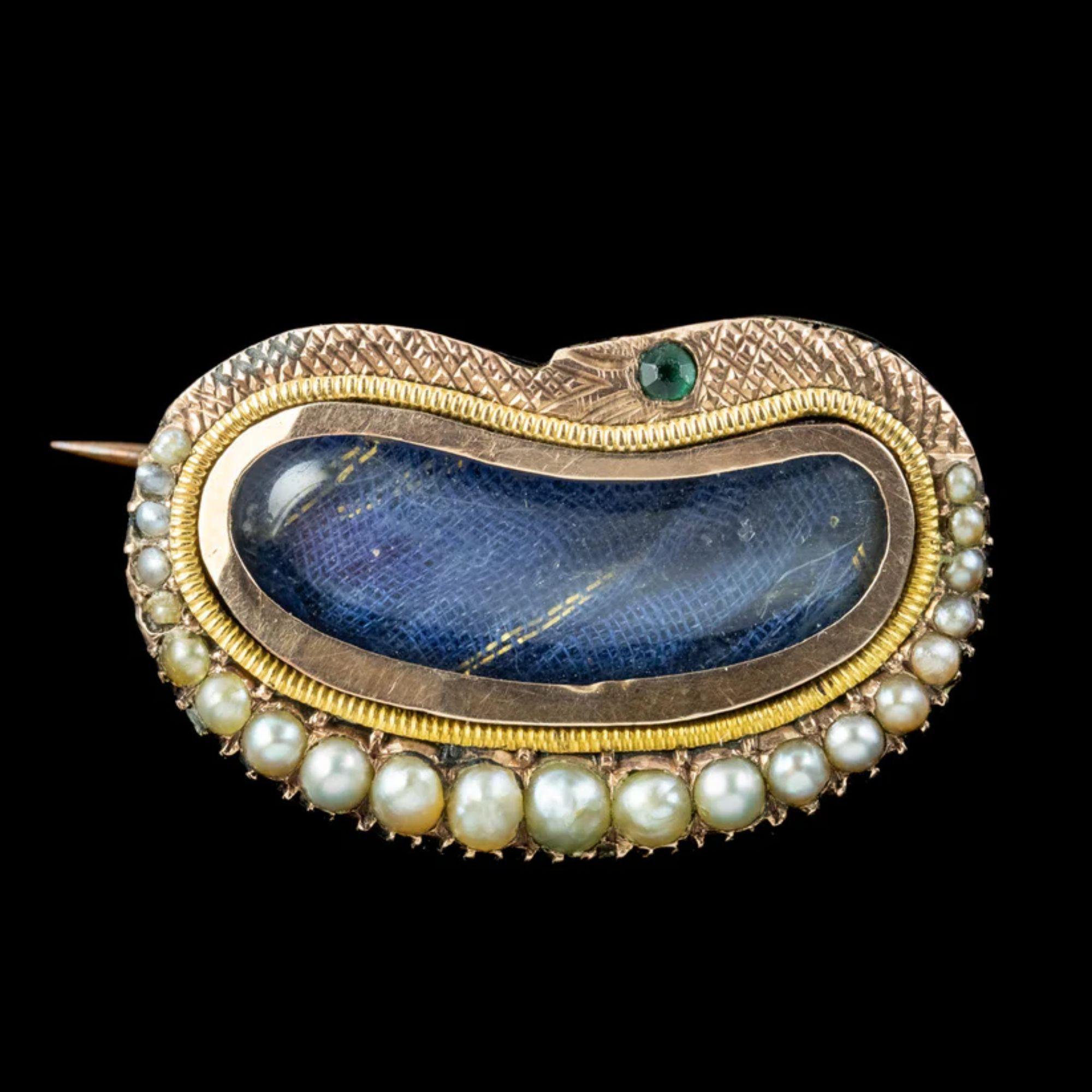 An exquisite antique Georgian mourning brooch from the early 1800s featuring a bean-shaped window in the centre, with blue silk backing that would have traditionally held a lock of hair belonging to a deceased loved one so that a piece of them was