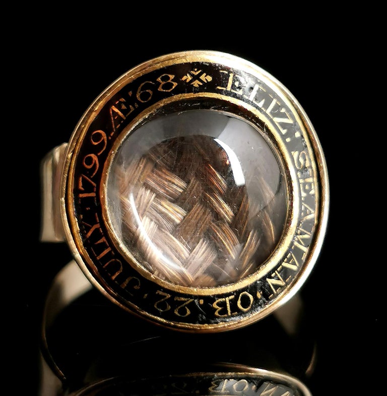 A beautiful antique Georgian era, late 18th century mourning ring.

It features a beautiful circular face housing a lock of finely plaited brown hair under the original convex glazing.

The domed crystal bordered by a ring of black enamel engraved