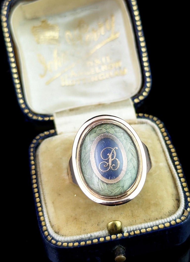 This beautiful antique Georgian era, late 18th century mourning ring is truly a beautifully crafted piece.

It features a beautiful large oval face housing a lock of plaited dark blonde hair bordering a cobalt blue enamel plaque with applied rose