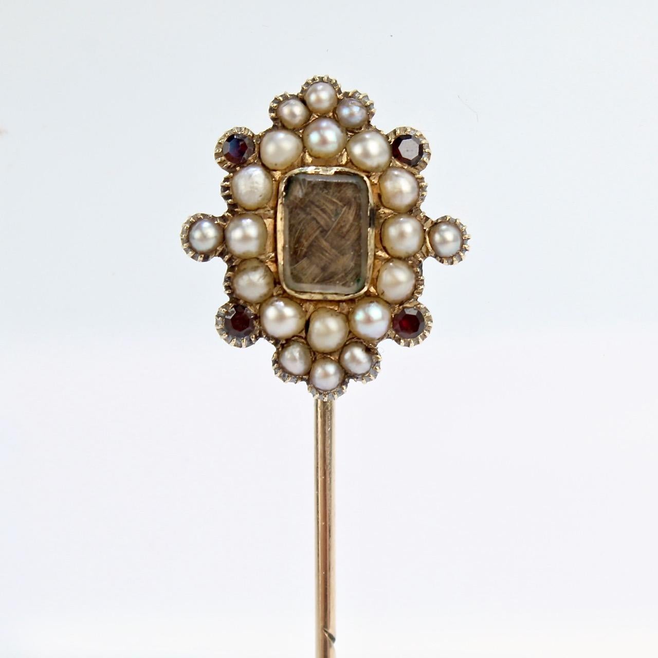 A fine Georgian hair art memorial or mourning stick pin.

With braided hair behind glass in a gold setting and surrounded by seed pearls and garnets. 

In the Georgian and Victorian eras, woven hair art was used to memorialize a departed loved one
