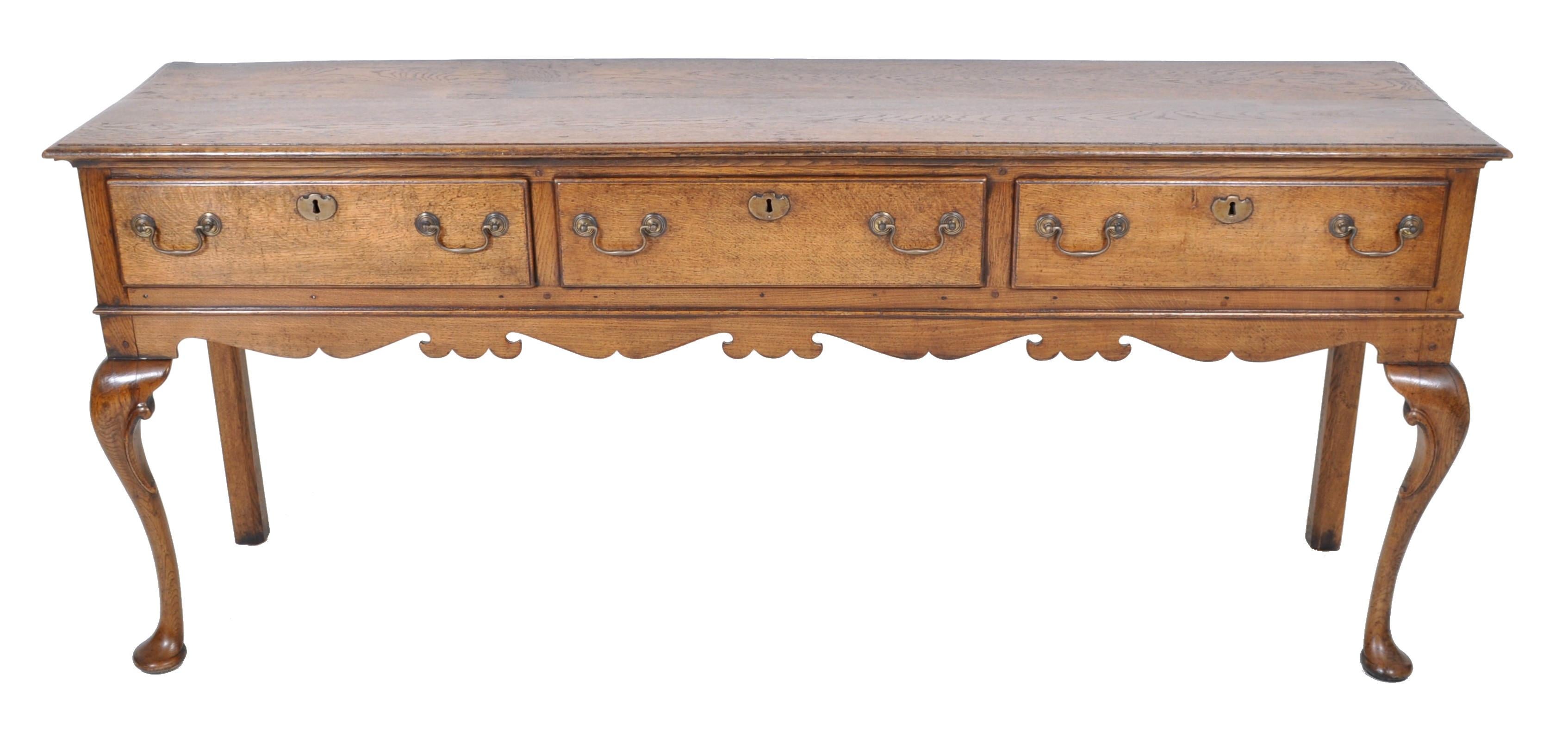 Antique Georgian oak dresser base, circa 1800. The dresser having an overhanging molded top, below three drawers with the original brass handles and escutcheons. The dresser standing on cabriole legs joined by a shaped skirt and terminating to pad