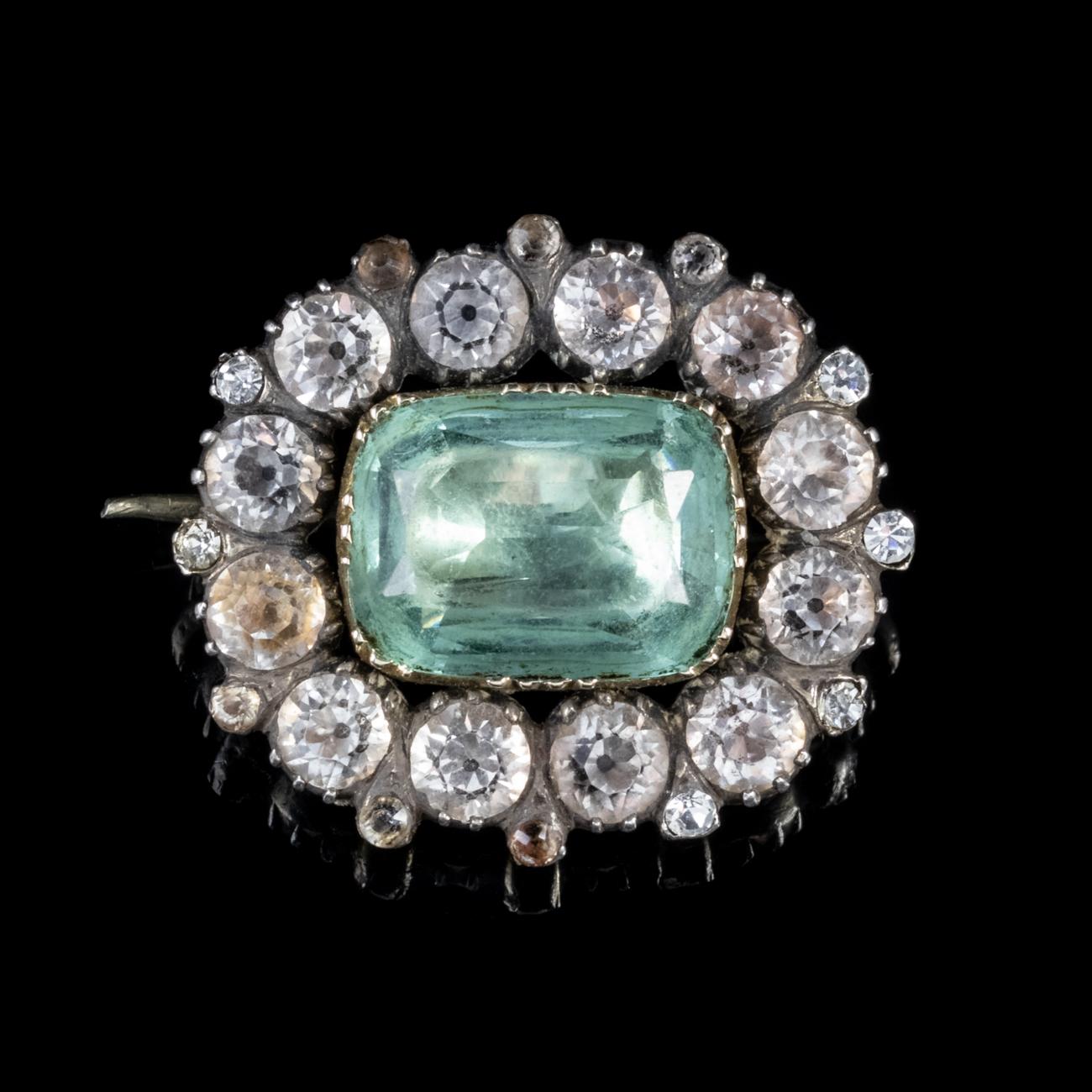 This stunning Antique Georgian brooch has been modelled in Silver and set with an array of Paste stones. It features a gorgeous central blue Paste stone which is set in an 18ct Yellow Gold gallery and is surrounded by a halo of white Paste stones.