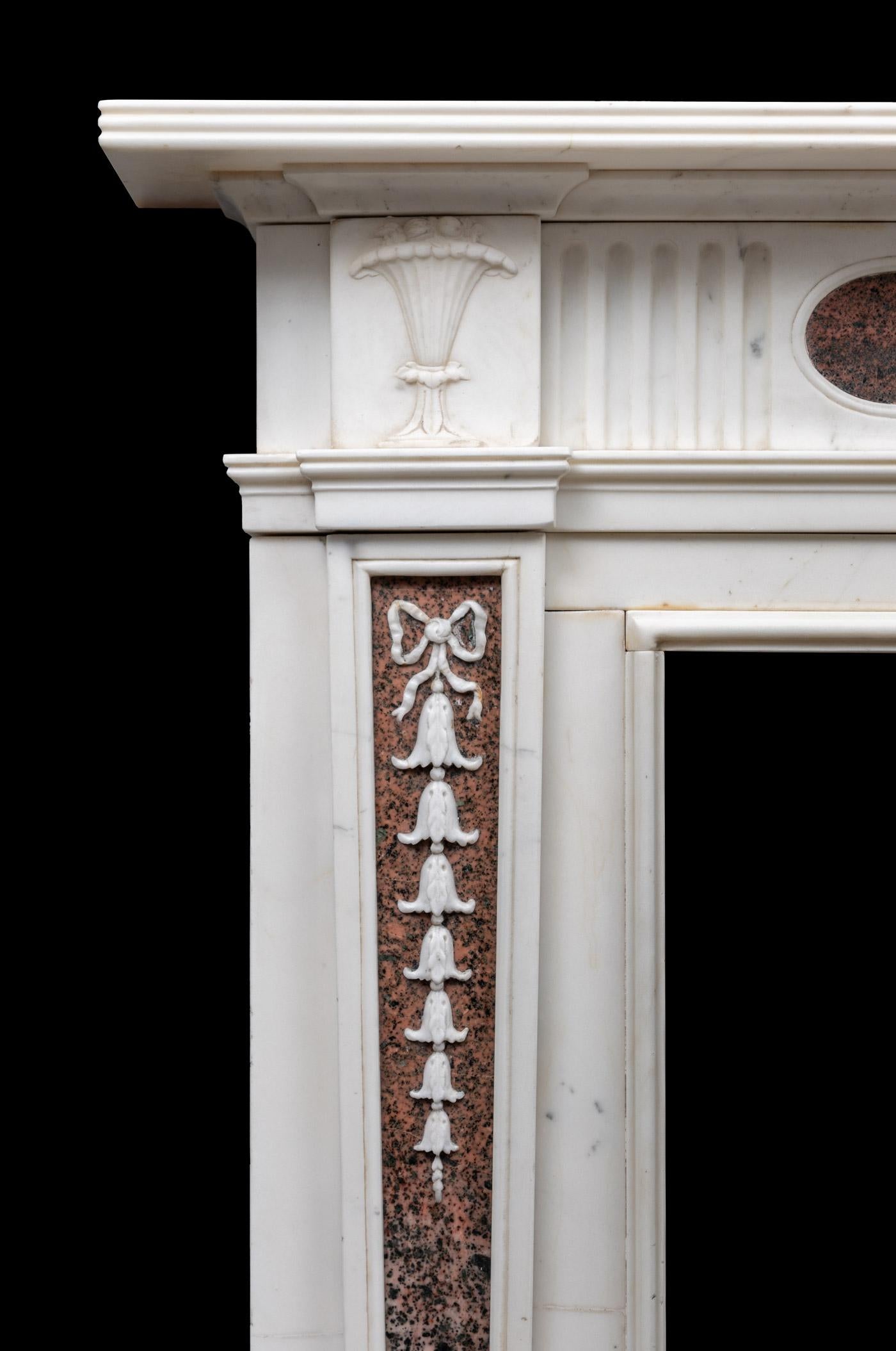 An antique neo-classical style marble chimneypiece from the late Georgian period.
The tapering pilasters are inlaid with panels of Scottish Isla Rosa Tiree marble and overlaid with carved bellflowers descending in size and upheld by bow ribbons.