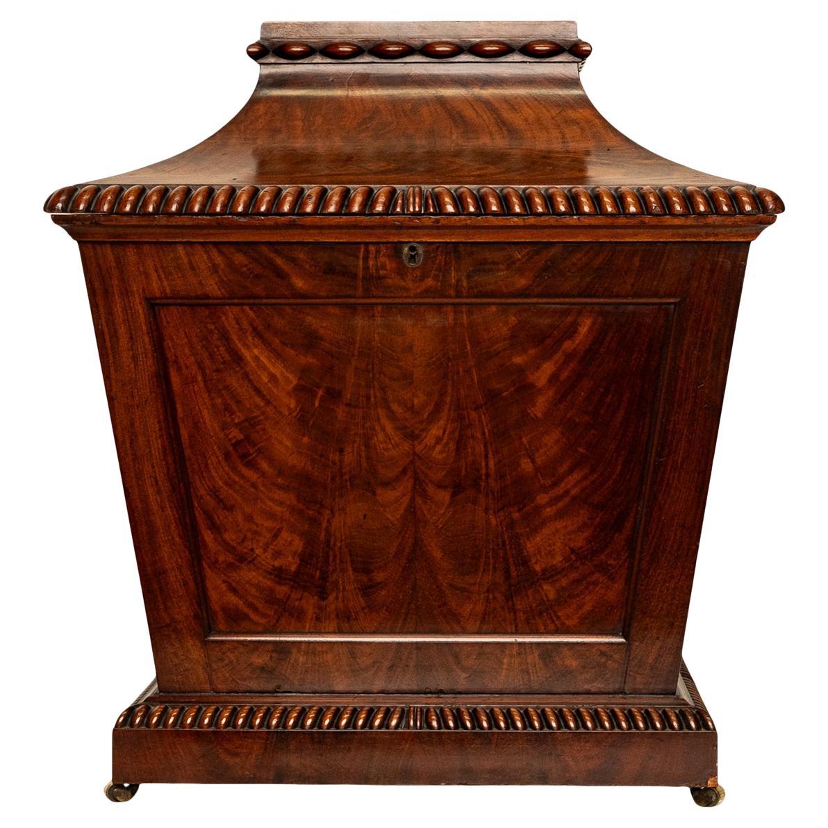 Antigua bodega o enfriador de vino de caoba de la Regencia Georgiana, hacia 1820.
El sótano, en forma de sacófago, tiene una banda de decoración eplipital tallada en la parte superior y un borde estriado en la tapa abatible; la base, inclinada y