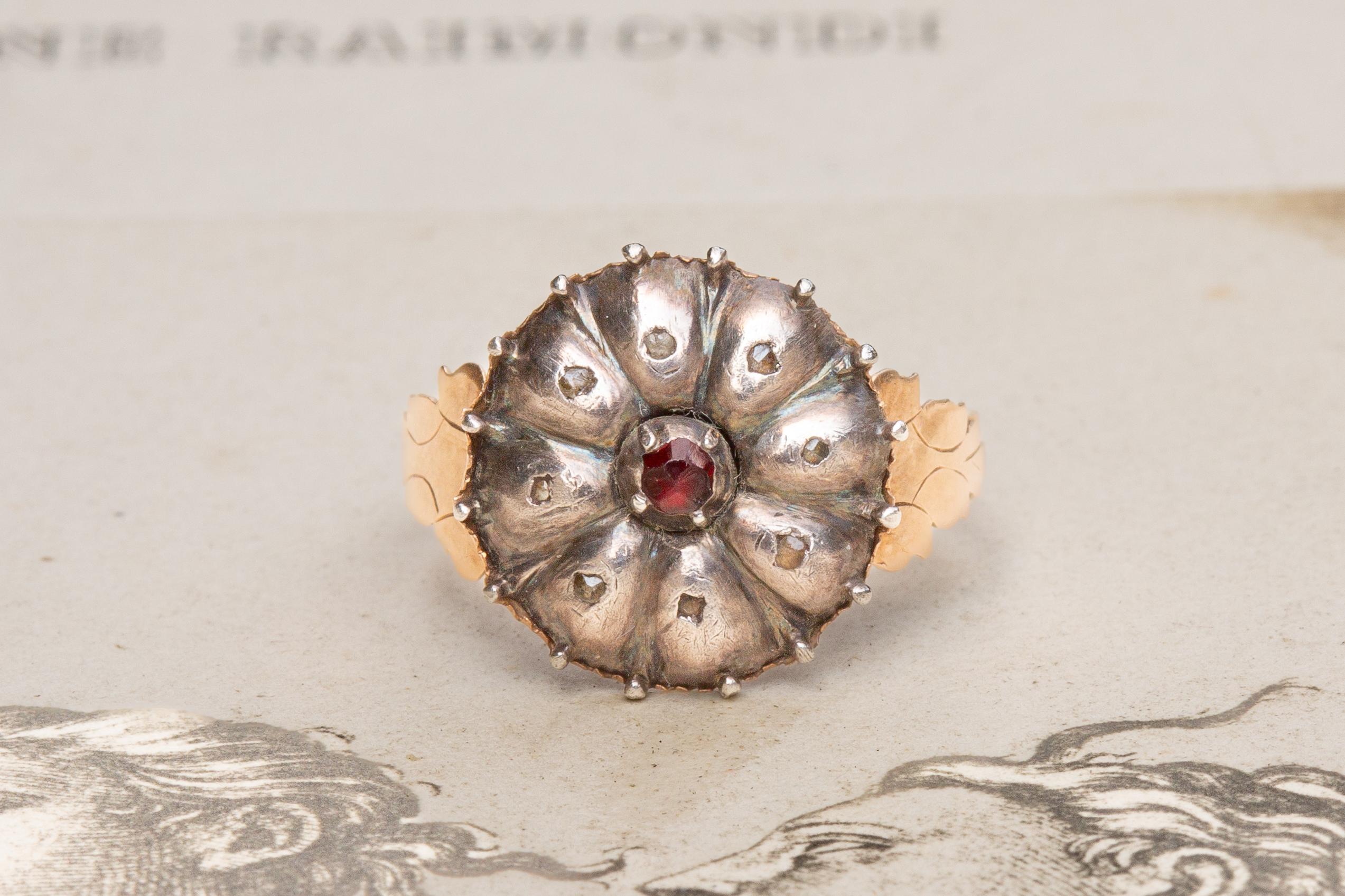This lovely antique cluster ring dates to around 1800 and was made in either Southern Germany or Italy. In the middle of the ring head lies a red garnet, surrounded by a cluster of 8 rose cut white topaz stones in rubover silver settings. 

The