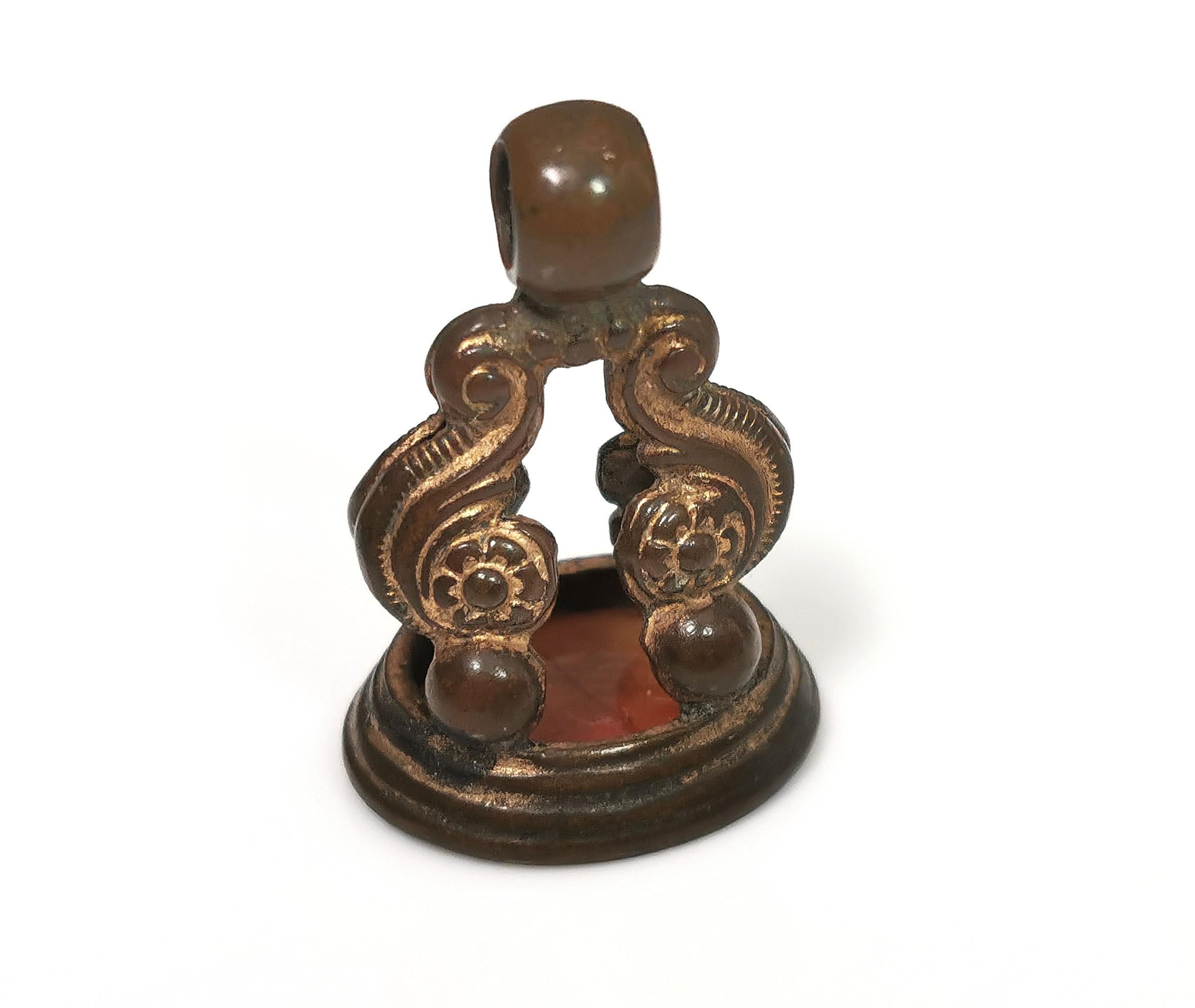 Un joli pendentif en forme de sceau, datant de l'époque géorgienne.

Fabriqué en bronze, il a un aspect rustique et était autrefois doré à l'or fin, mais cette dorure a disparu.

Le bouton de sceau présente un motif d'arc à enroulement ouvert, que