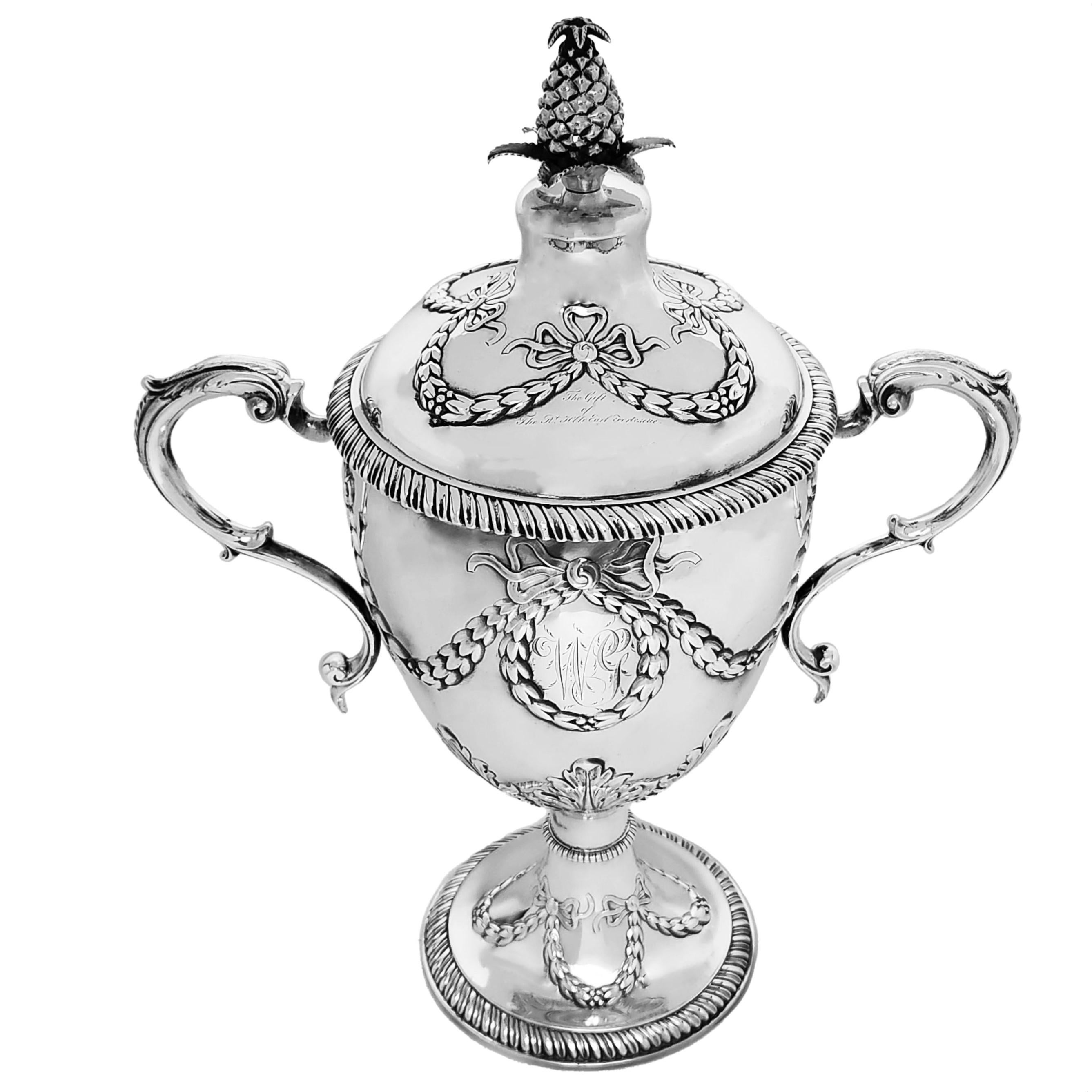 An Antique George III Sterling Silver Cup & Cover embellished with a classic swag and bow chased design. The Swags encircle oval cartouches on both sides of the trophy and each cartouche has a monogram engraved in the centre. The swag and bow design
