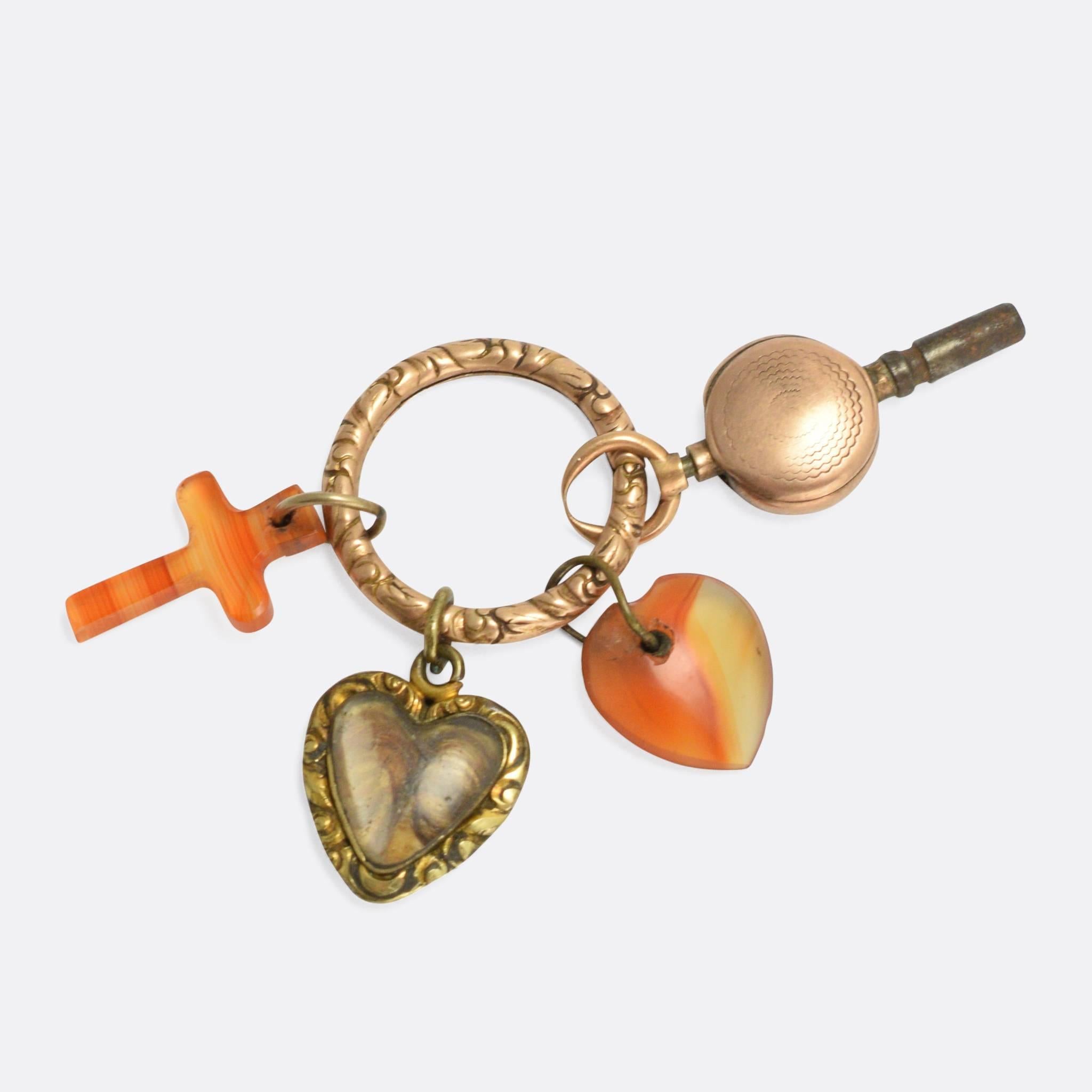 An ornate Georgian split ring, modelled in 15k gold and pre-loaded with period charms. Present are a cross and heart carved from carnelian, a pocket watch key, and a chased heart locket. The split ring makes a perfect charm holder, ready for your