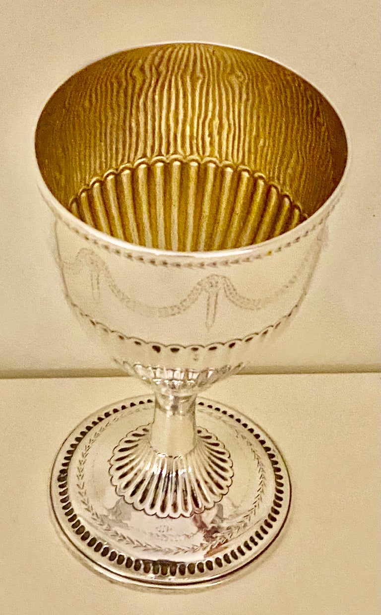 A very fine and handsome antique Georgian sterling silver goblet having a round body with hand-chased half-fluted decoration, with bright cut decoration with a gold-gilt interior, and sitting on a pedestal foot with a round base. Made in London in