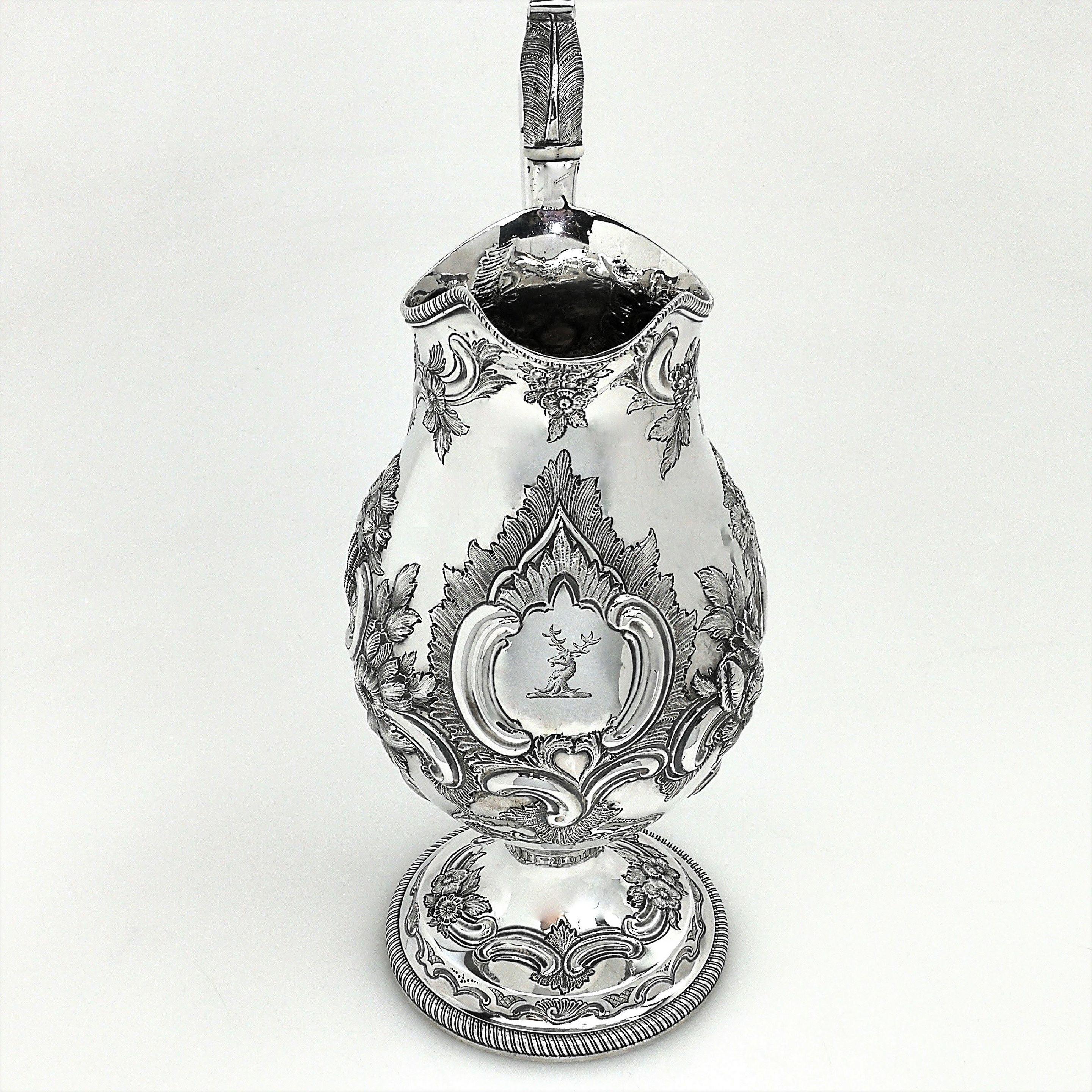 A beautiful Antique solid Silver Jug with in a classic baluster shape with a tall spread pedestal foot. The body and foot of the Jug are embellished with a detailed chased floral, foliate and scroll pattern and the Jug has a substantial acanthus