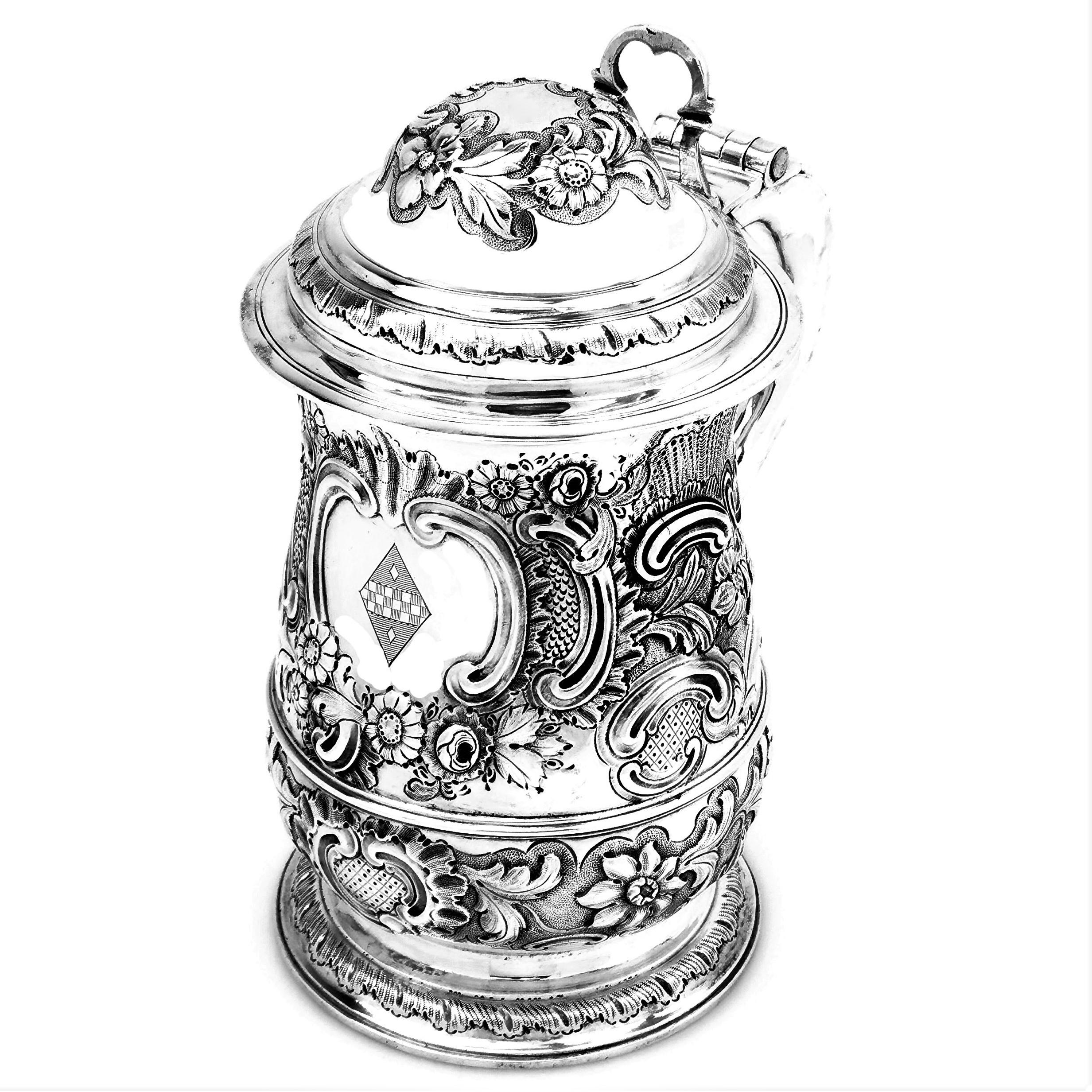 An impressive antique George III sterling silver Lidded Tankard embellished with an ornate chased design on the body, domed lid and spread foot. The body of the Tankard has an elegant floral and scroll design around a shaped cartouche with an