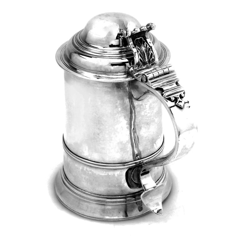 A classic Antique George III solid silver Lidded Tankard in a traditional straight sided design. The Tankard has a spread foot and a hinged domed lid and has an engraved crest and monogram opposite the substantial scroll handle. The Tankard has a