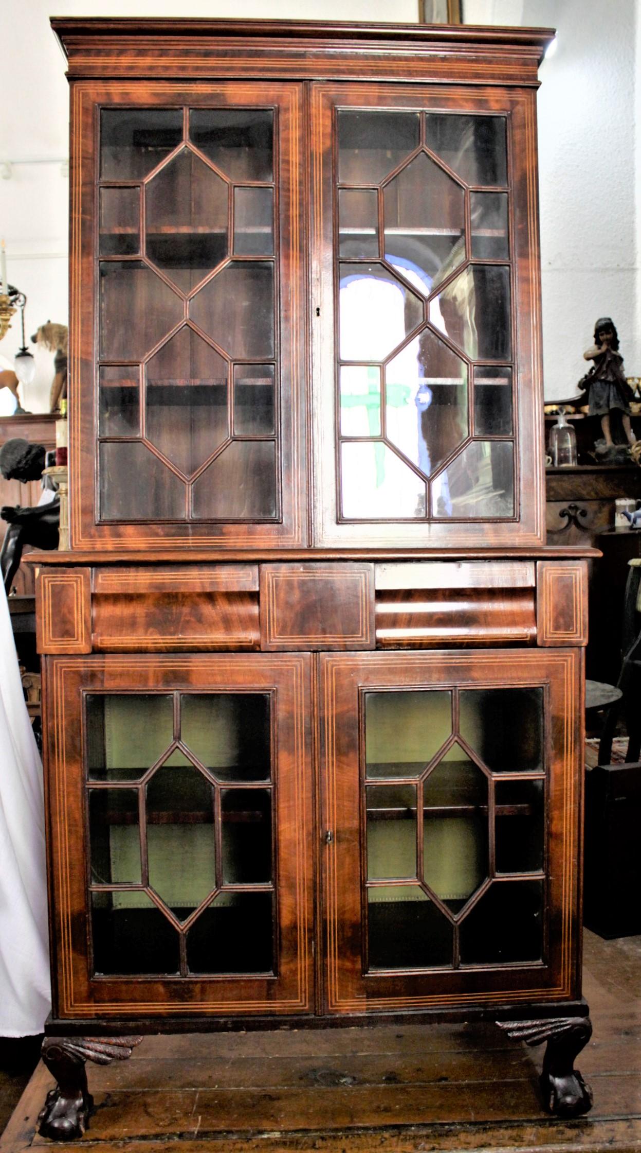 This antique mahogany bookcase cabinet if unsigned but presumed to have been made in England in circa 1880 in the Georgian style. The bookcase has four locking doors with nice thick fretwork and astral glazed glass. The front is inlaid with ebony