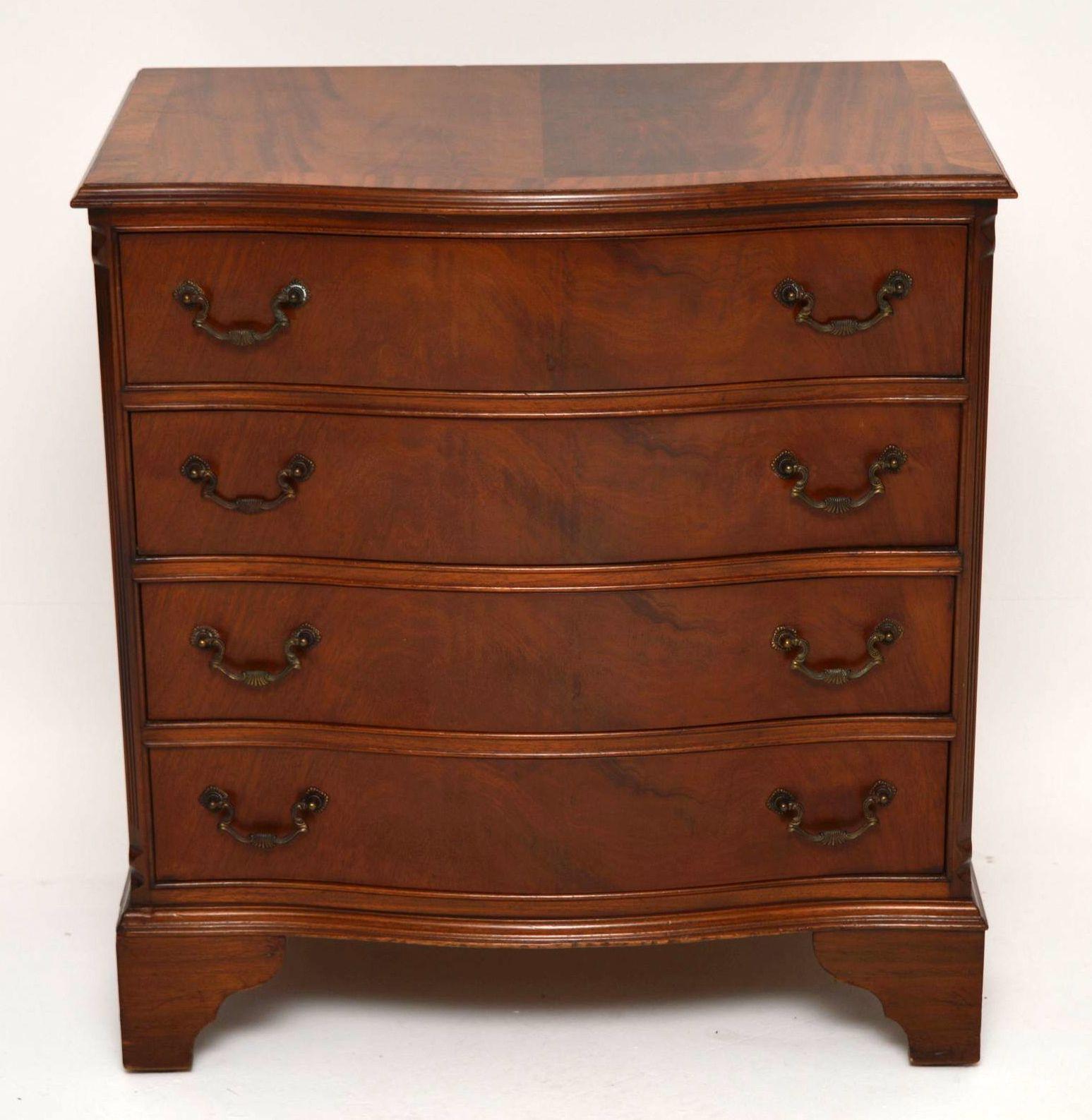 Antique Georgian style flame mahogany chest of drawers with a serpentine shaped front, in excellent condition dating from circa 1950s period. It has a cross banded top, four drawers with original brass handles, reeded canted corners and sits on