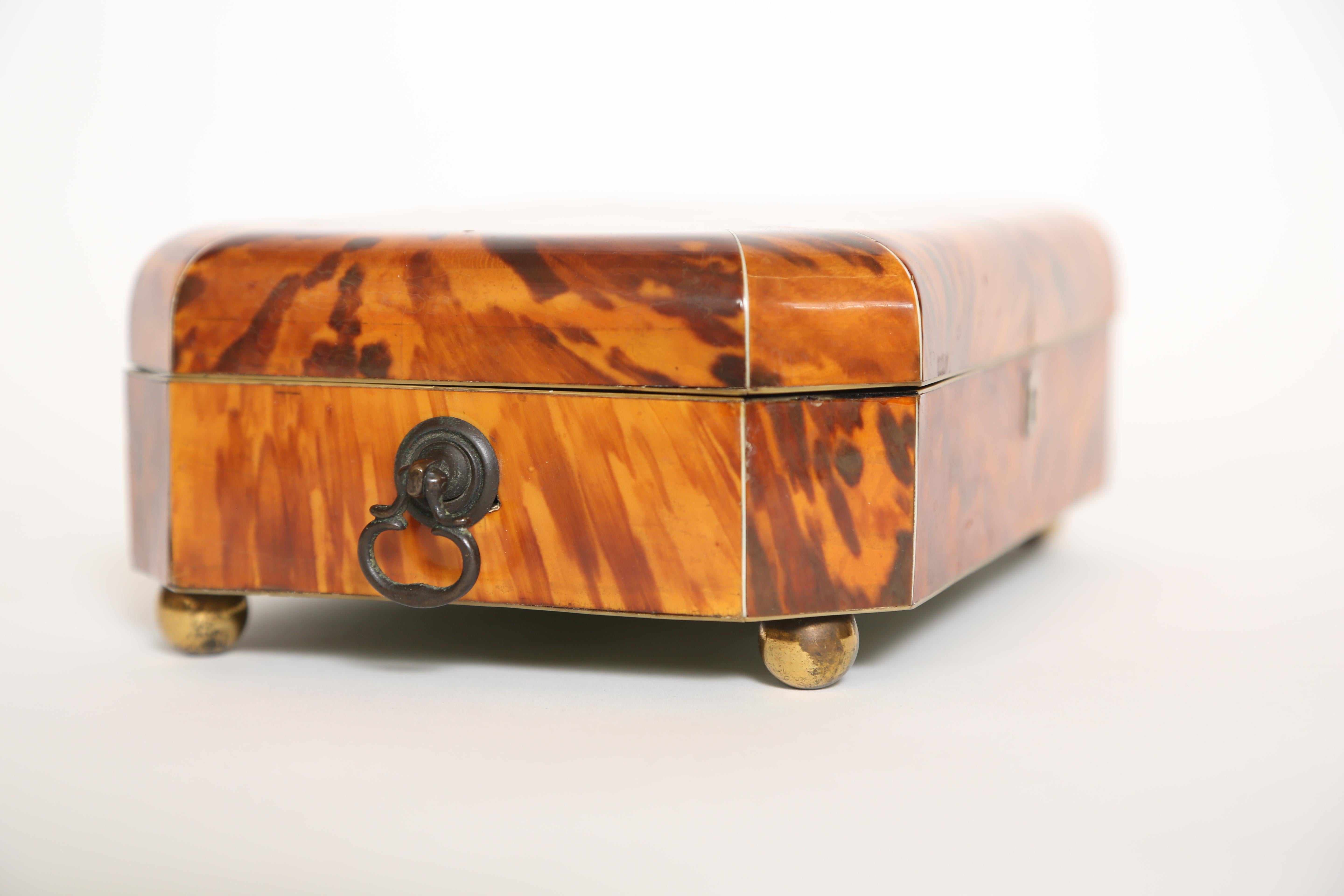 Antique Georgian tortoiseshell jewelry box with brass handles and ball feet. The outer surface is covered with bookmatched panels. The interior was newly relined.

(This item is eligible for a gift box)